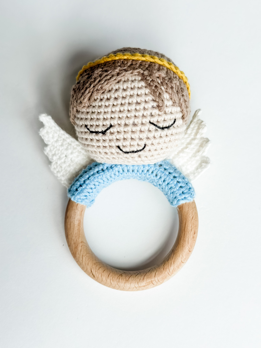 Crocheted angel rattle with wooden ring on a light gray background
