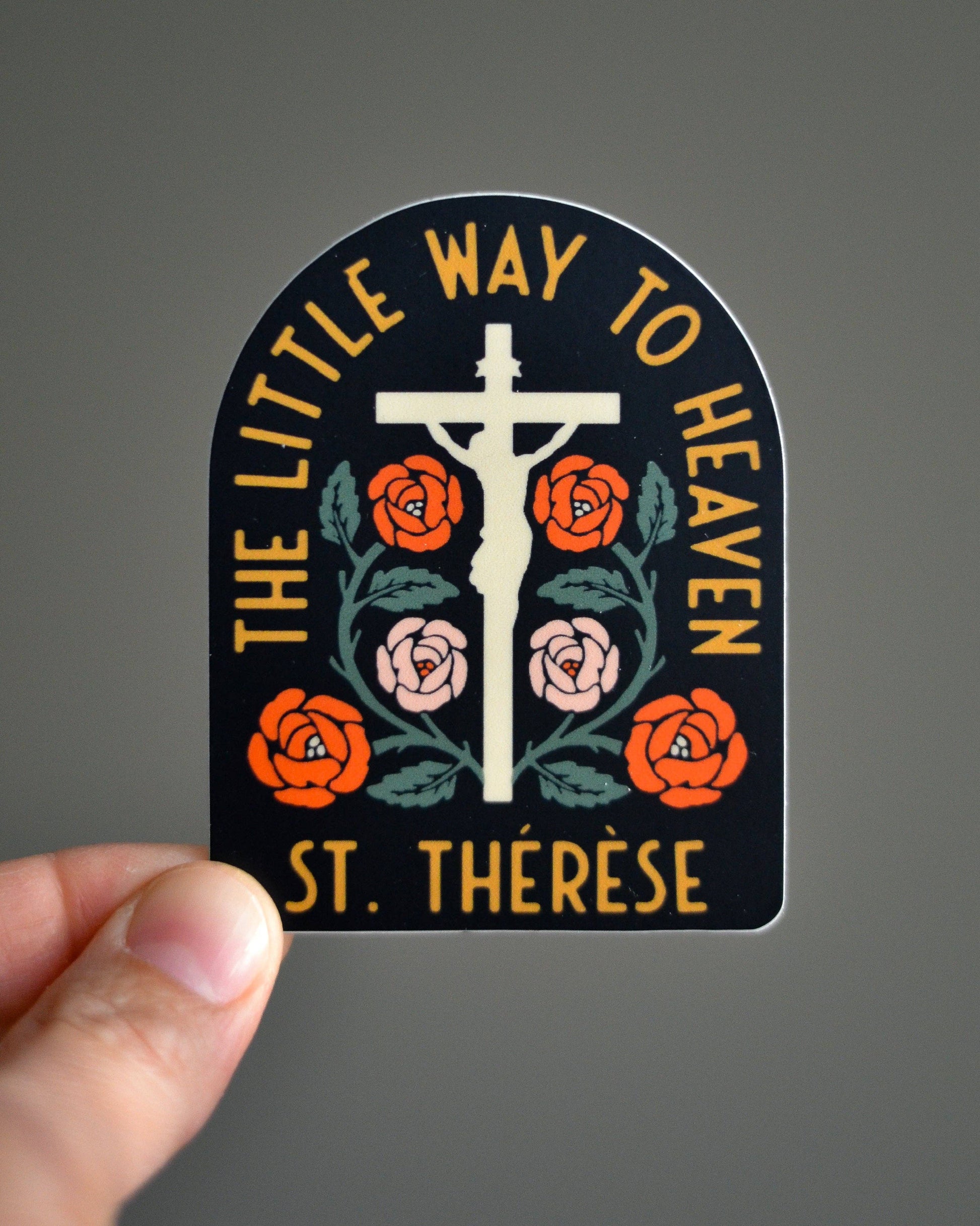 Sticker with cross and flowers design held by a hand against a gray background