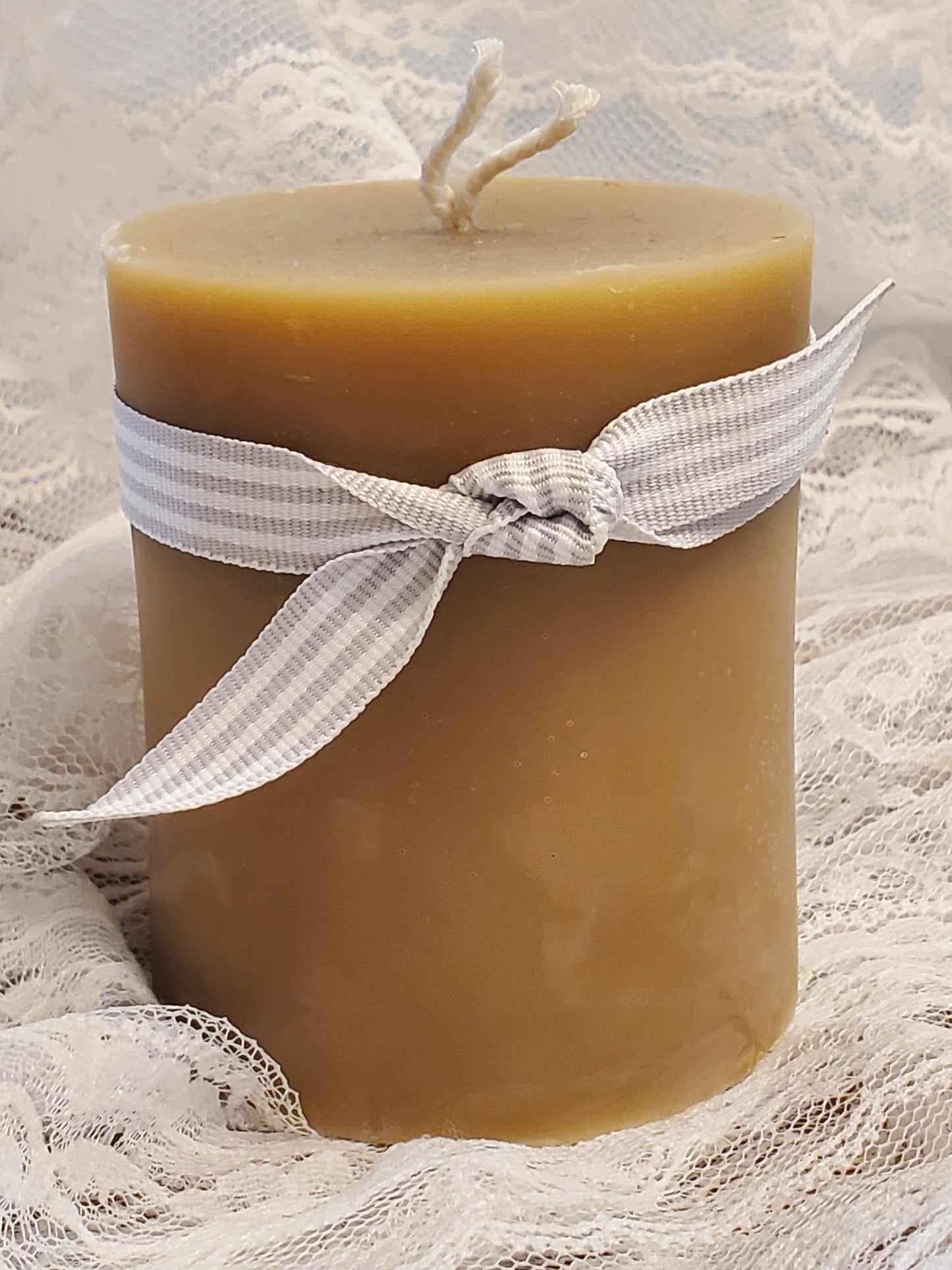 Beeswax candle with a white ribbon on a textured beige background