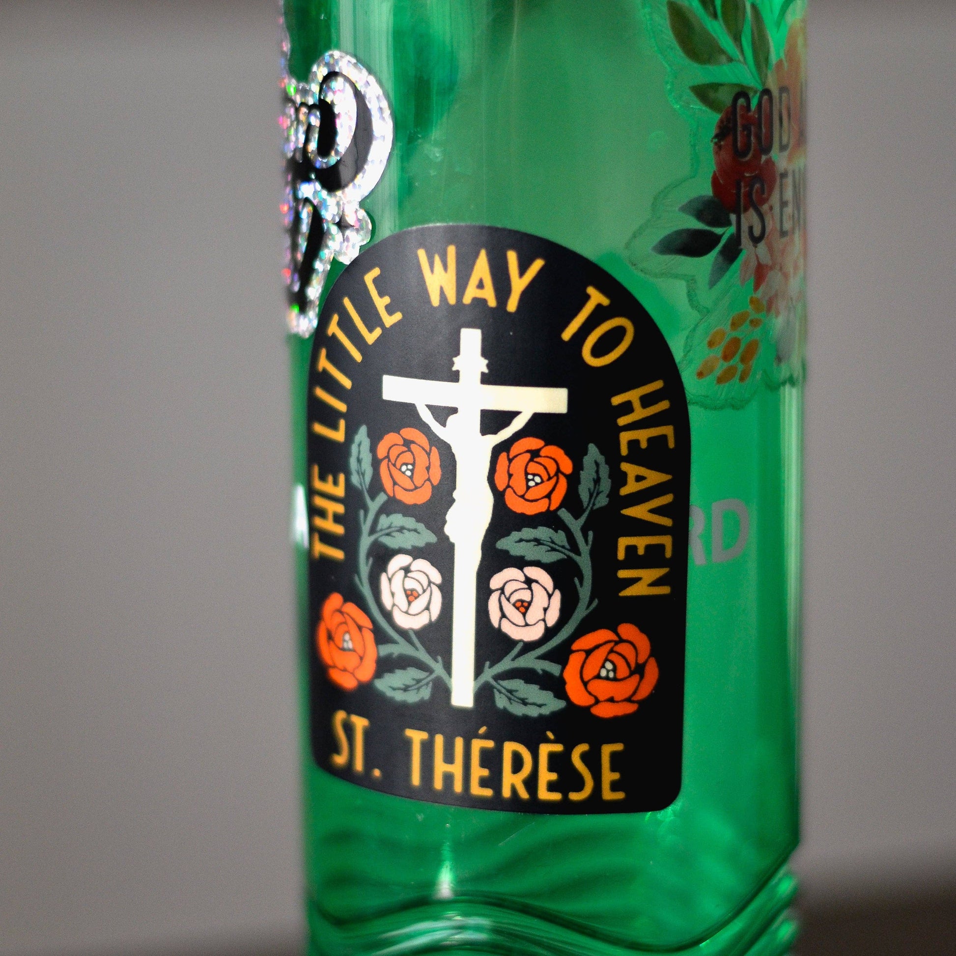 Green bottle with 'The Little Way to Heaven St. Therese' label on a gray background