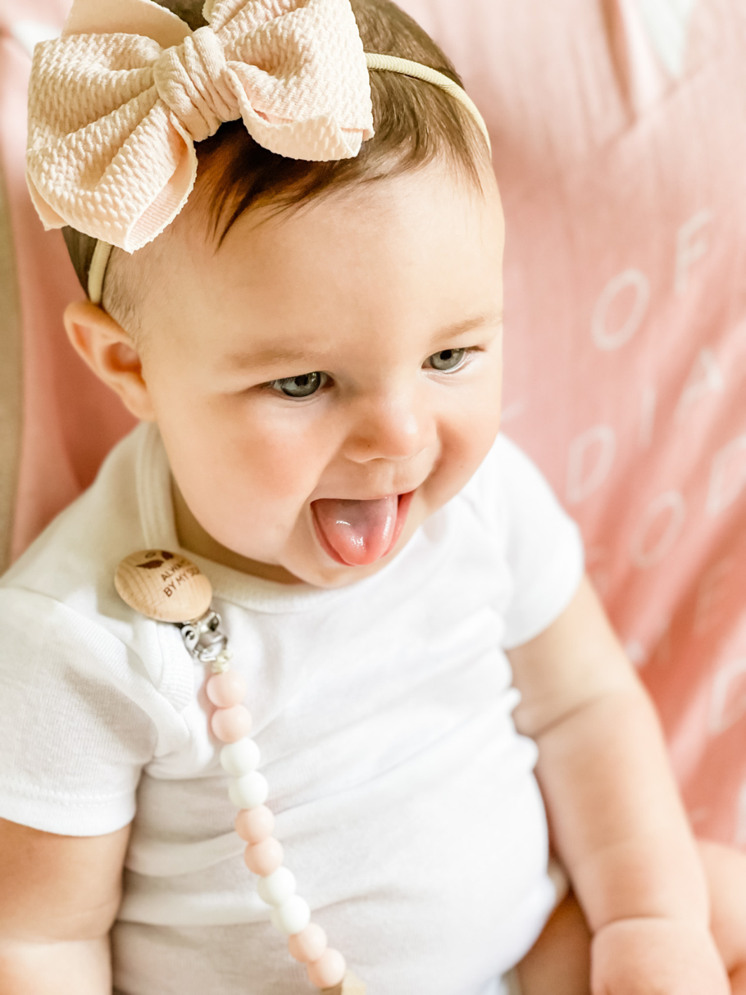 Baby with a bow headband and white outfit against a pink background