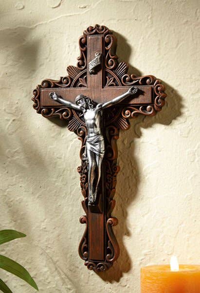 Wooden cross with a figurine of Jesus on a beige wall with a candle.