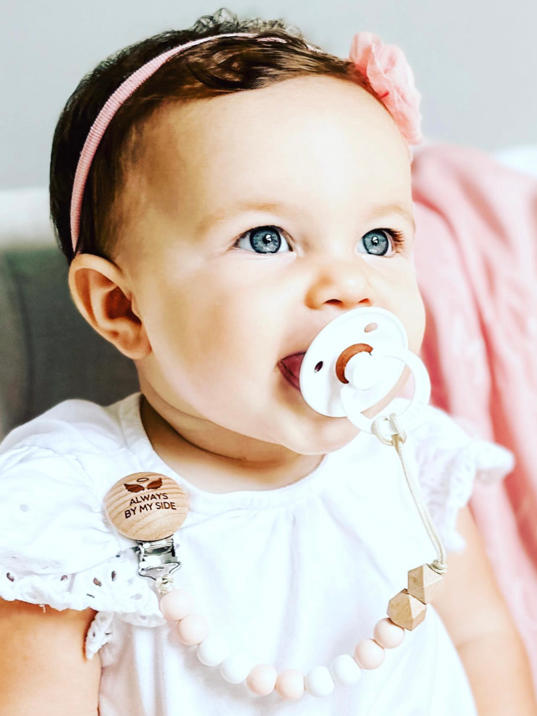 Baby with a pacifier and pink headband against a light background