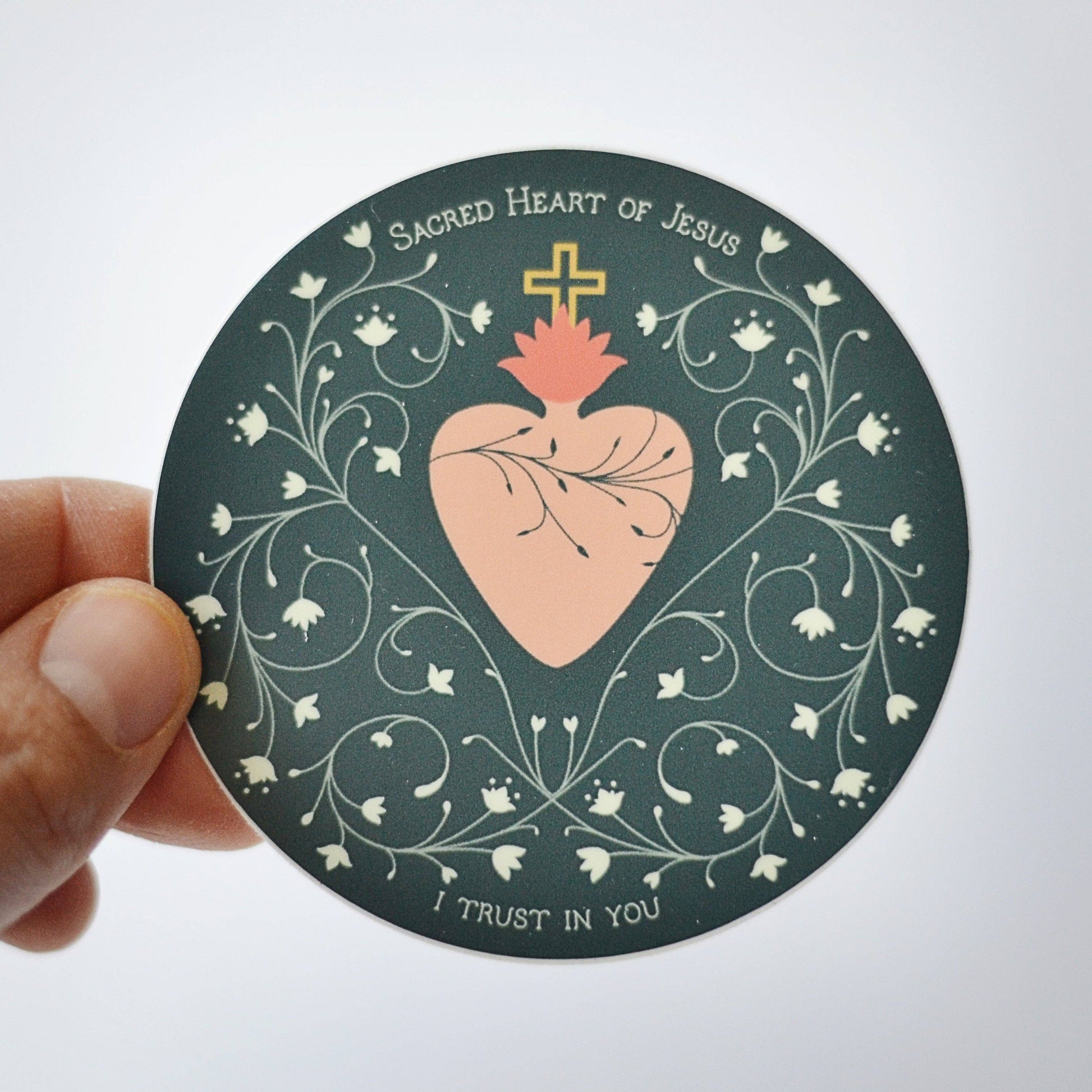 Circular sticker with Sacred Heart of Jesus design held by a hand on a white background