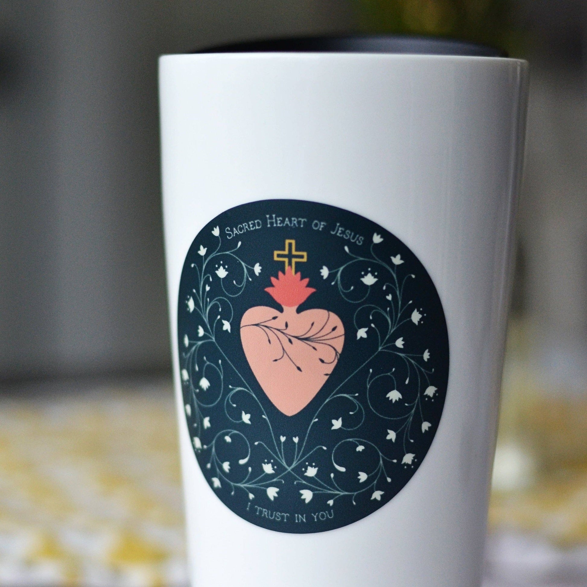 White tumbler with a 'Sacred Heart of Jesus' design on a blurred background