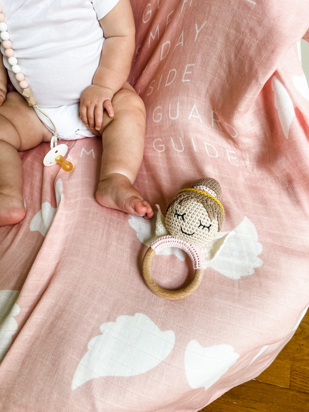 Baby's hand holding a soft toy on a pink blanket with cloud patterns