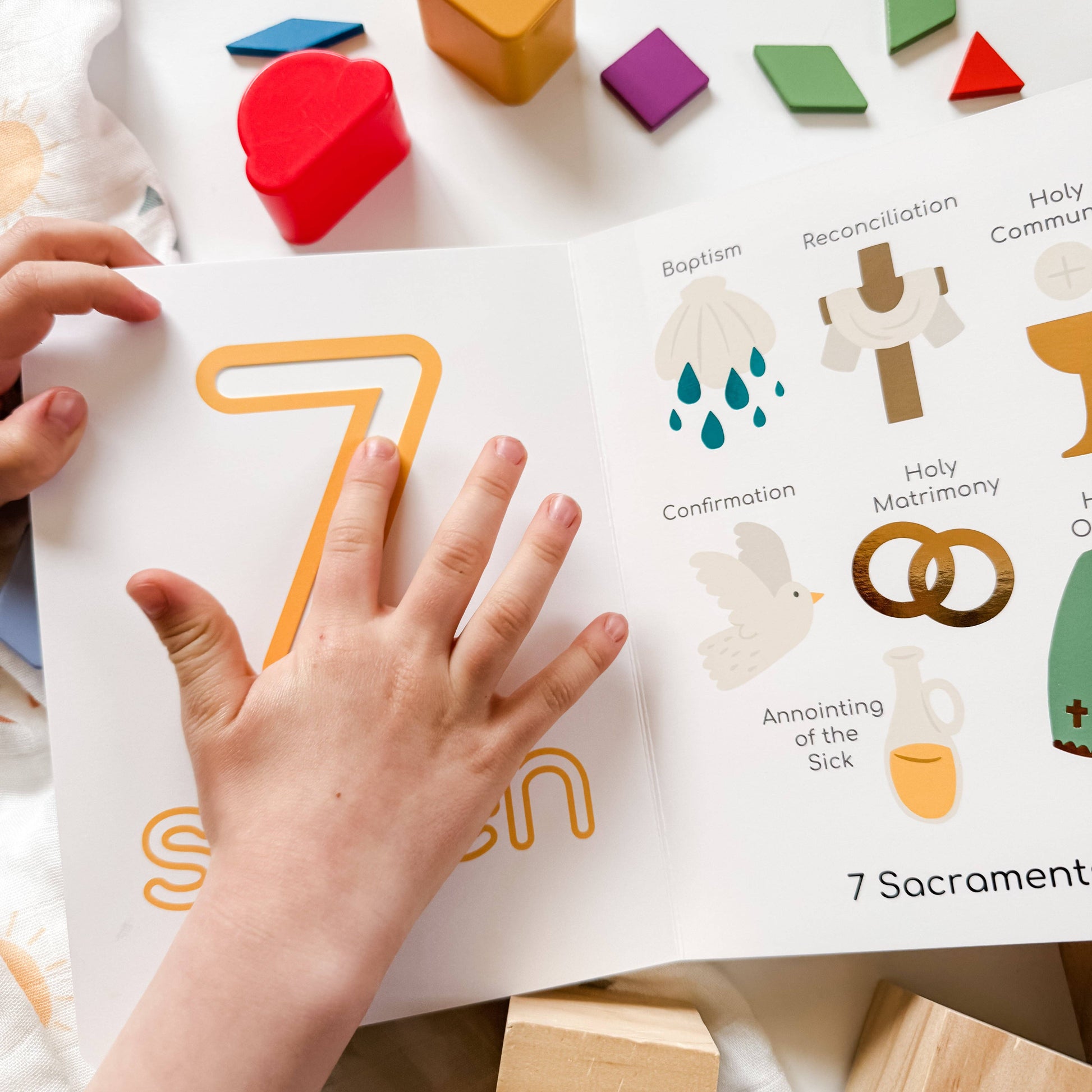 Child's hand pointing to the number '7' on a religious education material with sacramental symbols.