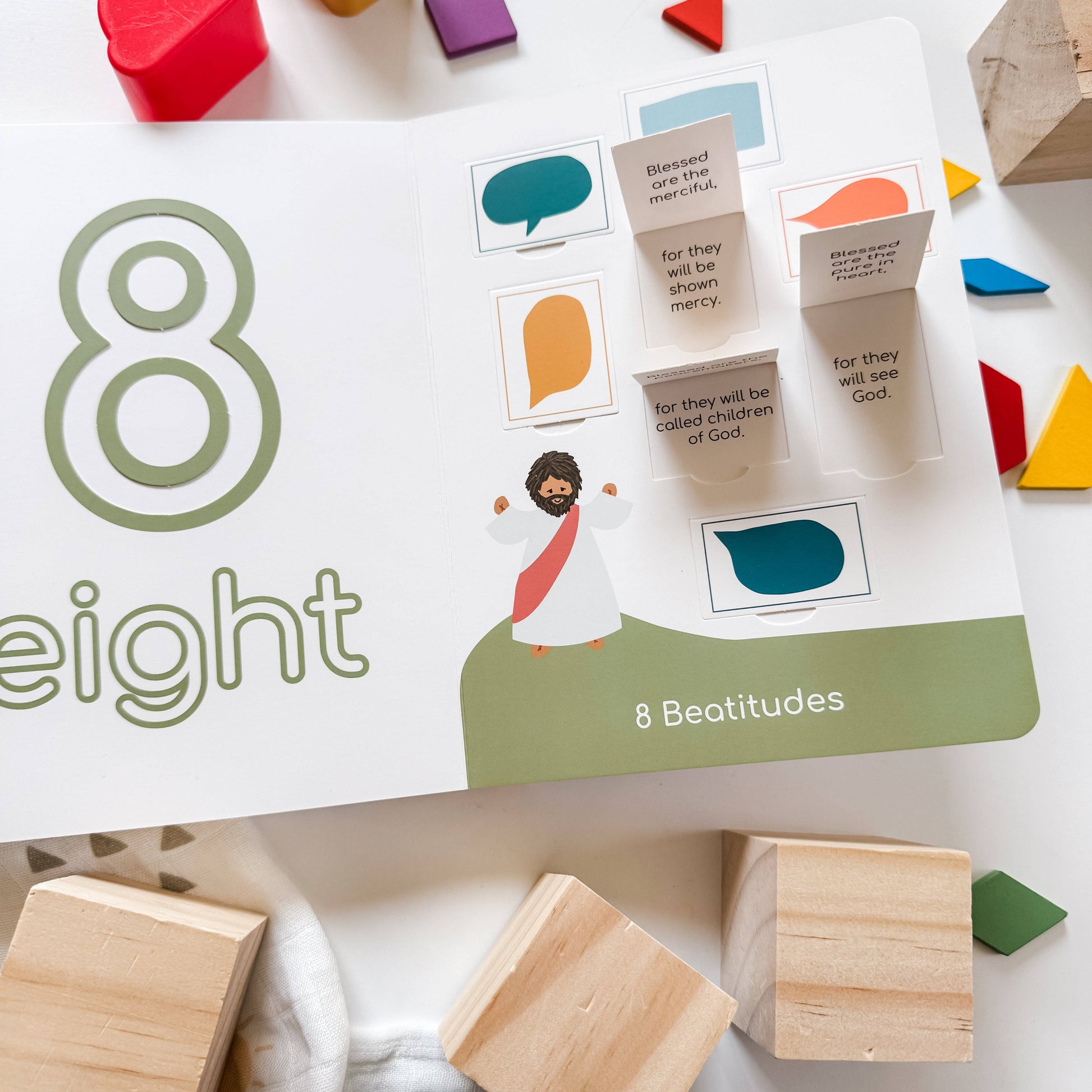 Educational card game titled 'Eight Beatitudes' with wooden blocks and colorful shapes on a white surface.