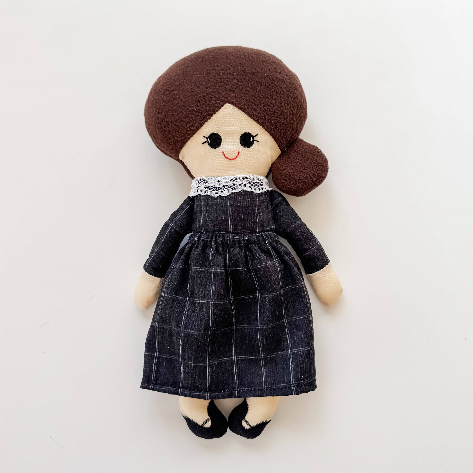 Plush doll with brown hair and a black checkered dress on a white background