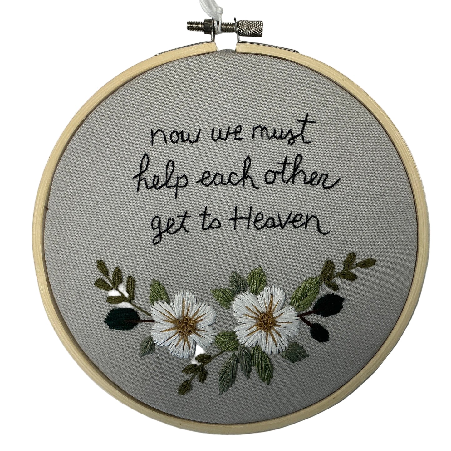 Embroidery hoop with text 'now we must help each other get to Heaven' and floral design on a gray background.