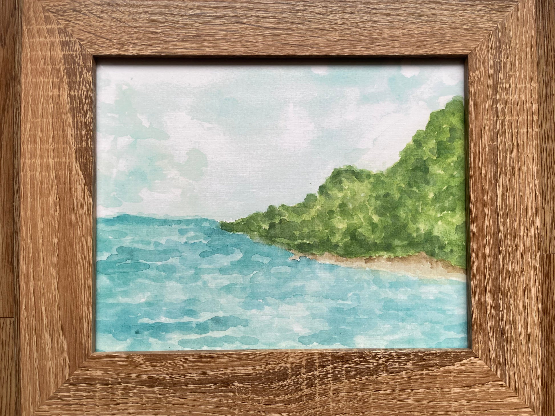 Framed artwork of a coastal scene with water and greenery.