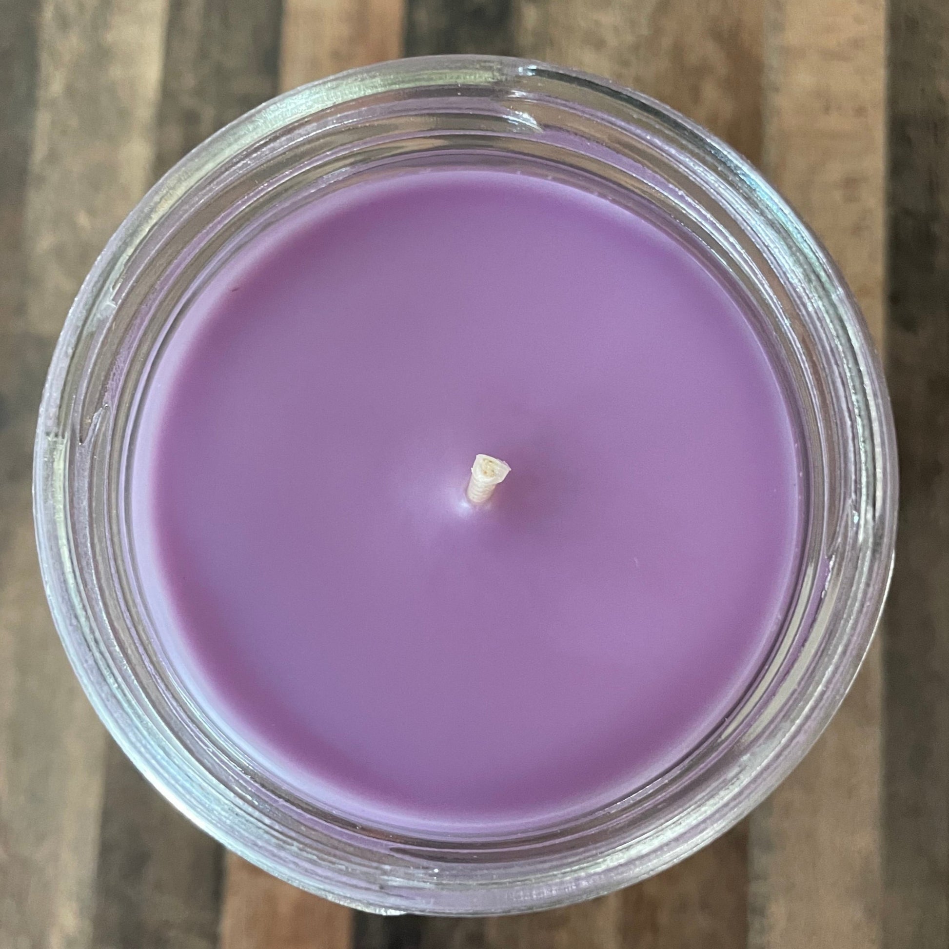 Purple candle in a glass jar on a wooden surface