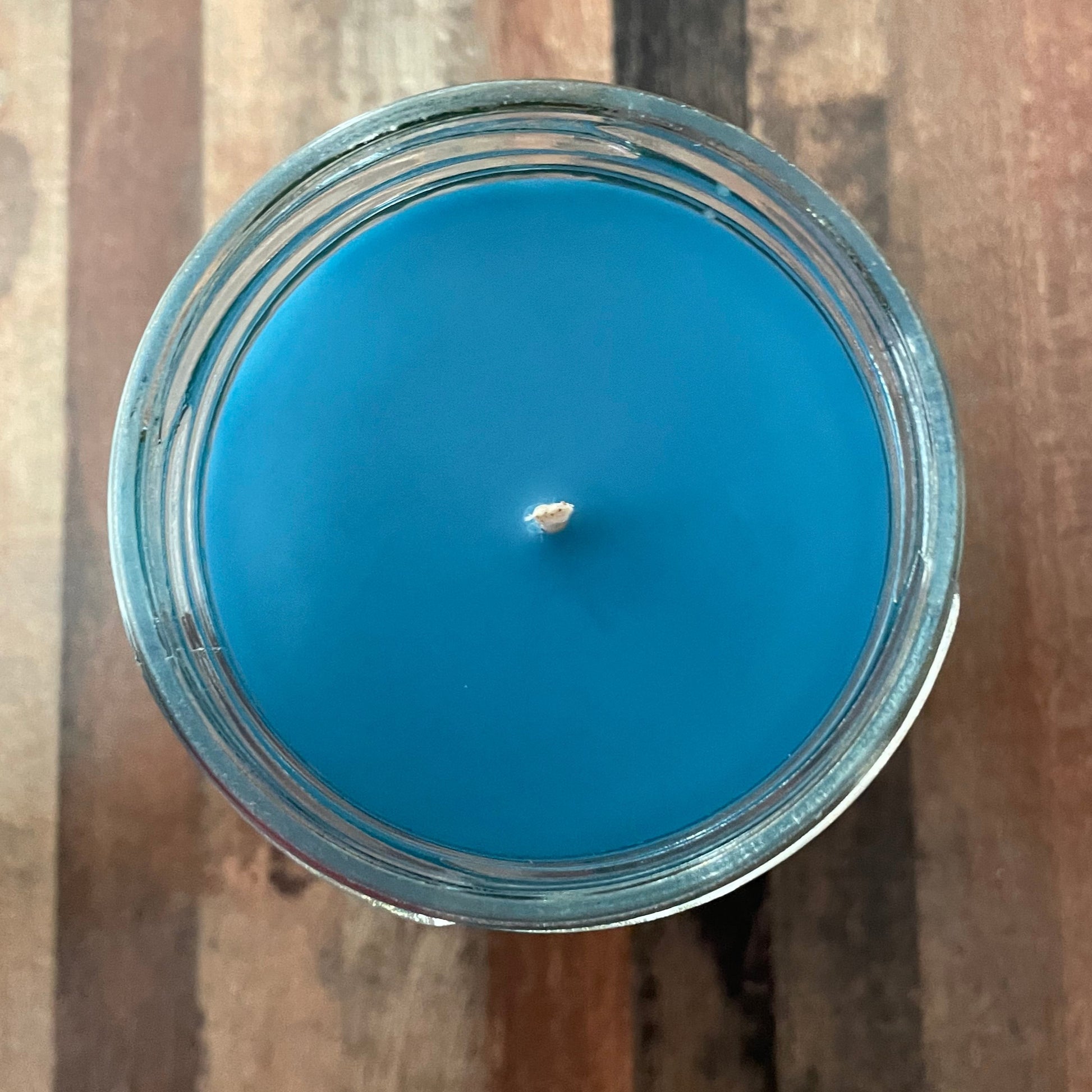 Blue candle in a glass container on a wooden surface