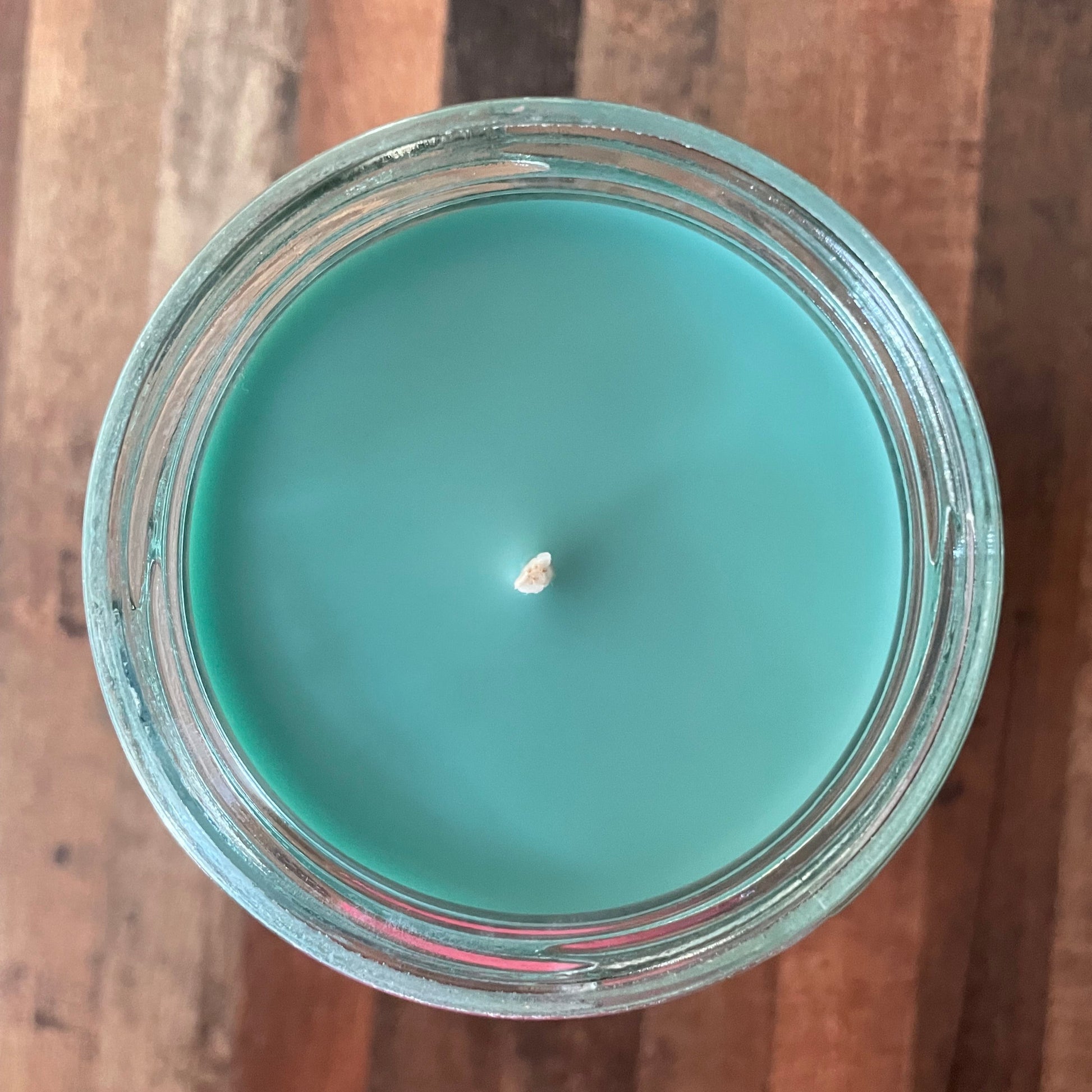 Teal candle in a clear glass jar on a wooden surface