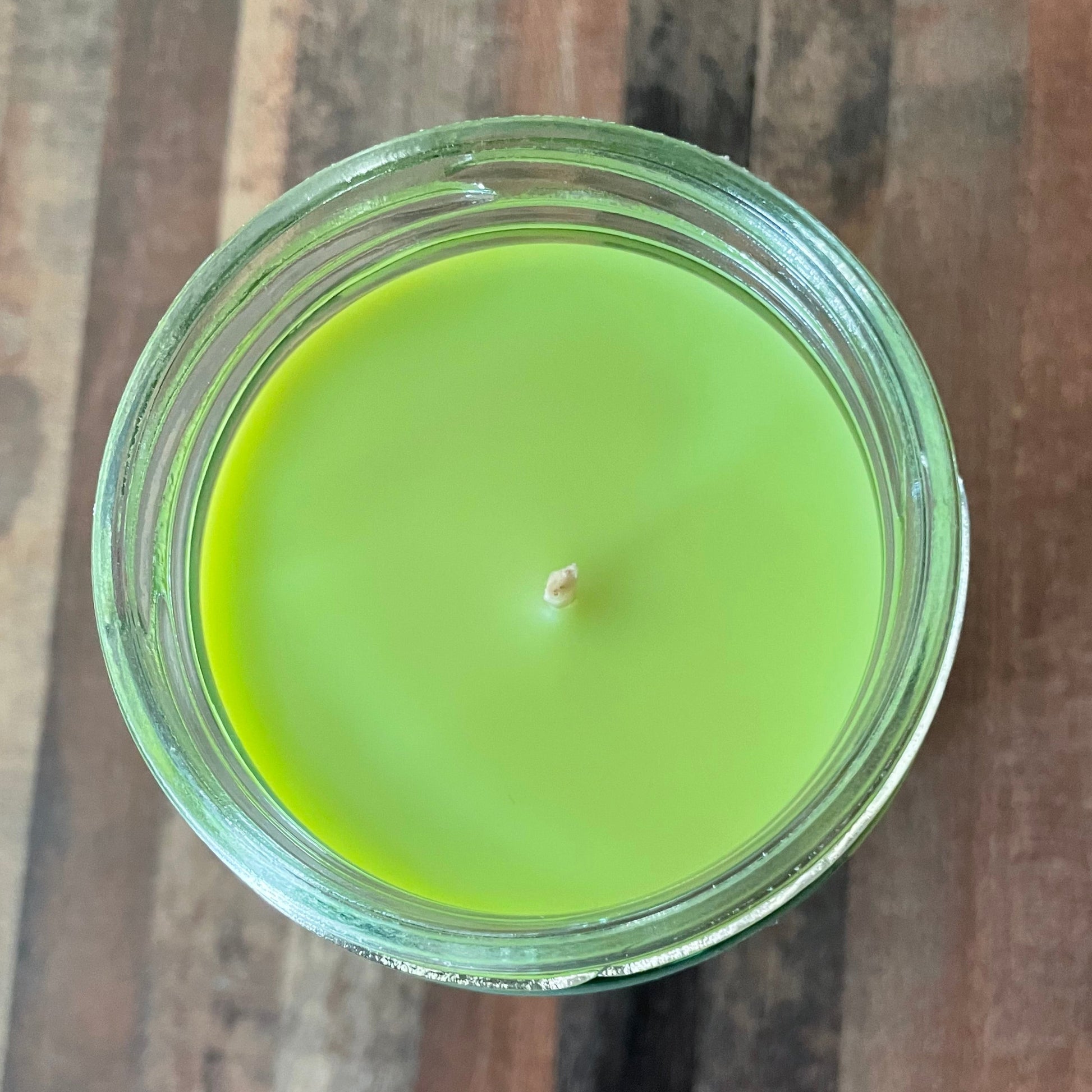 Green candle in a glass jar on a wooden surface
