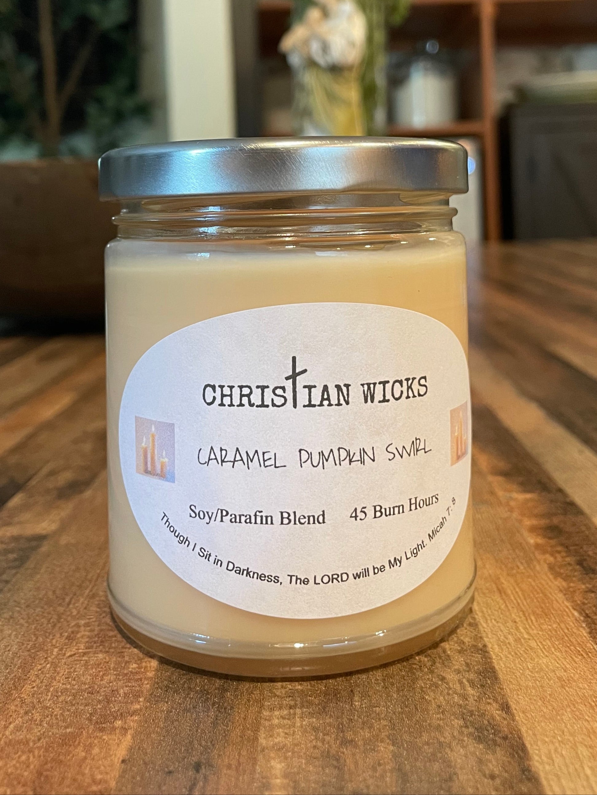 Jar of Christian Wicks caramel pumpkin swirl candle on a wooden surface with a blurred background