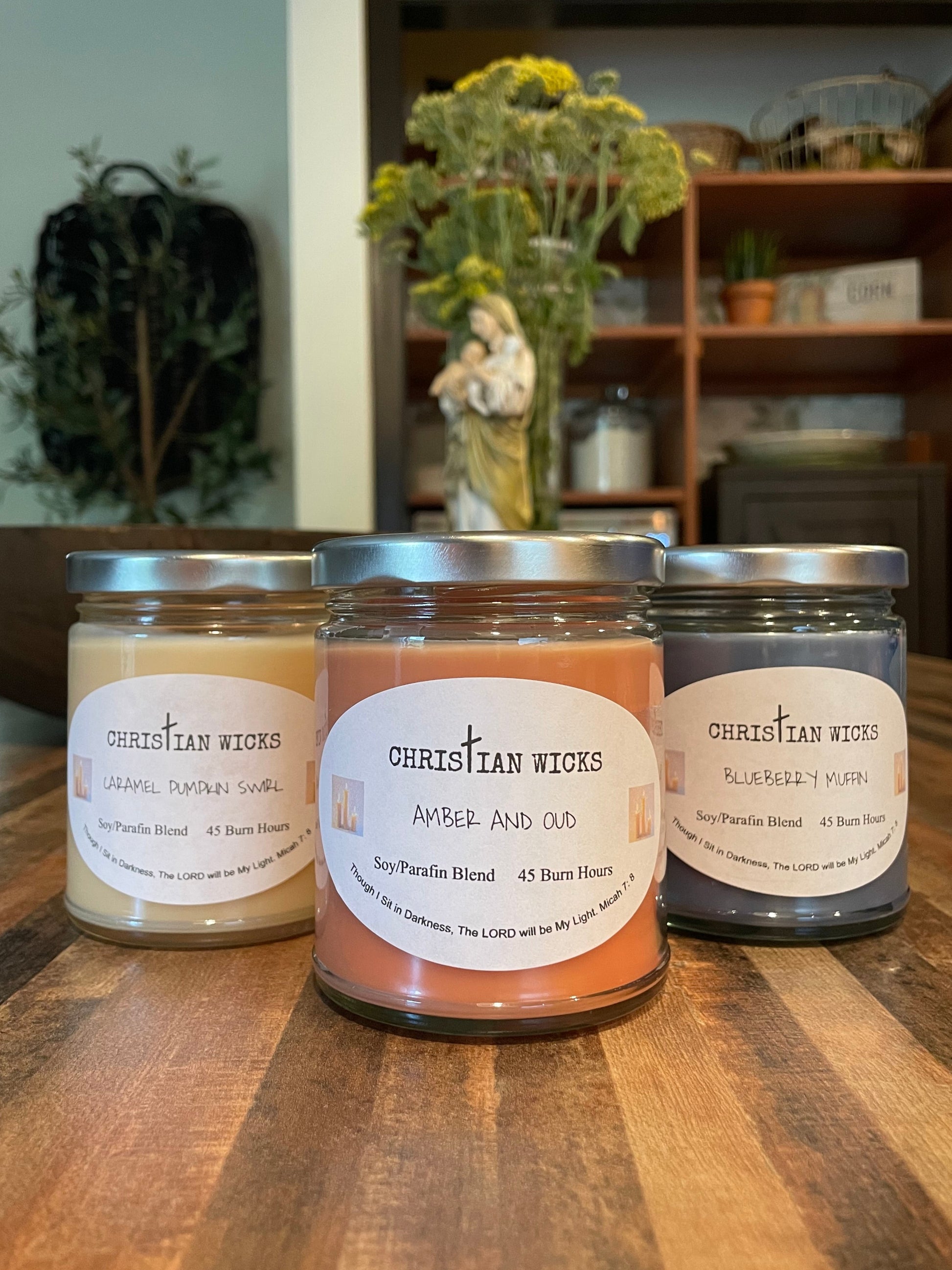 Three candles with labels on a wooden surface, with a blurred indoor background.