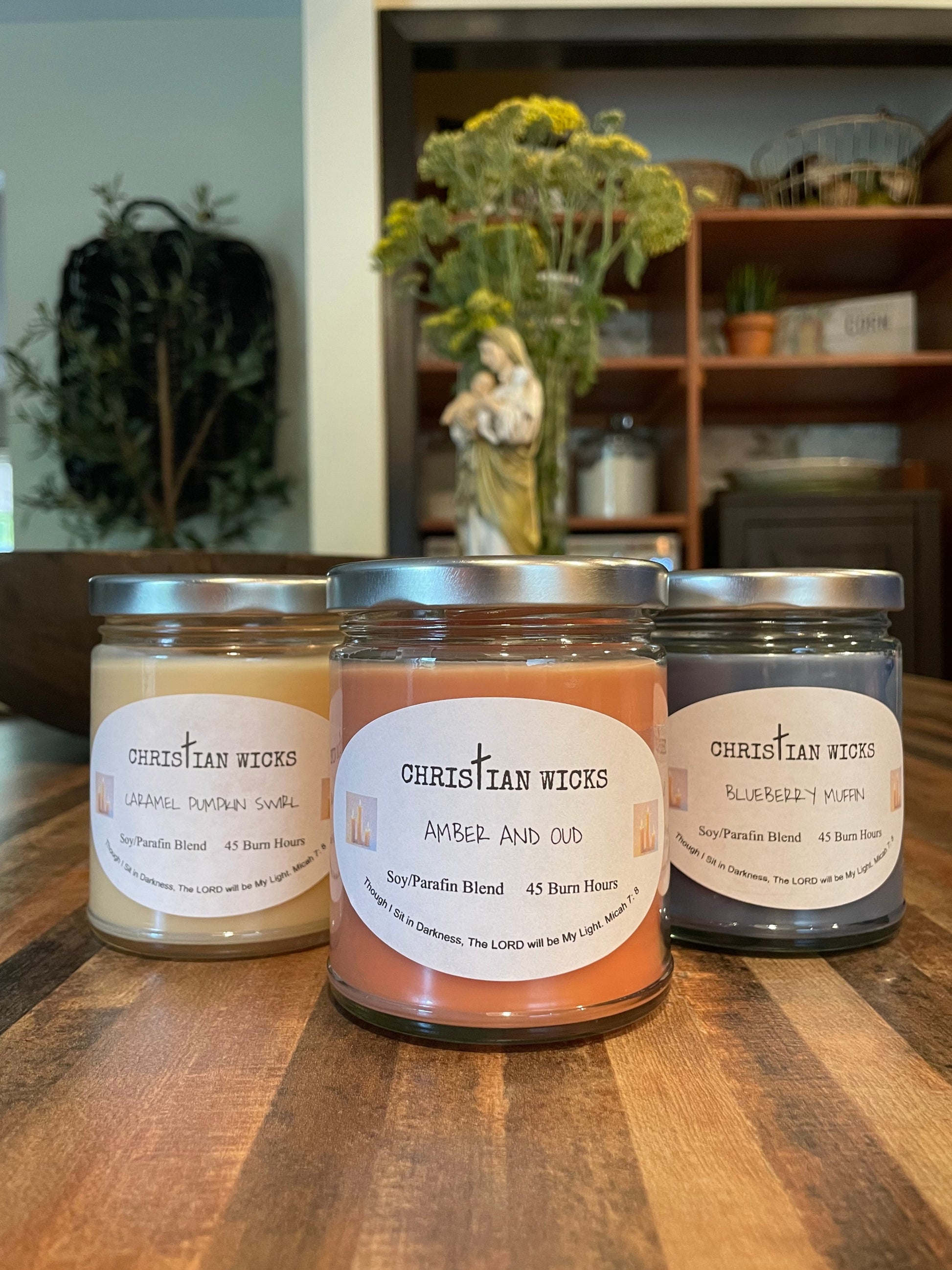 Three candles with labels on a wooden surface, with a blurred indoor background.