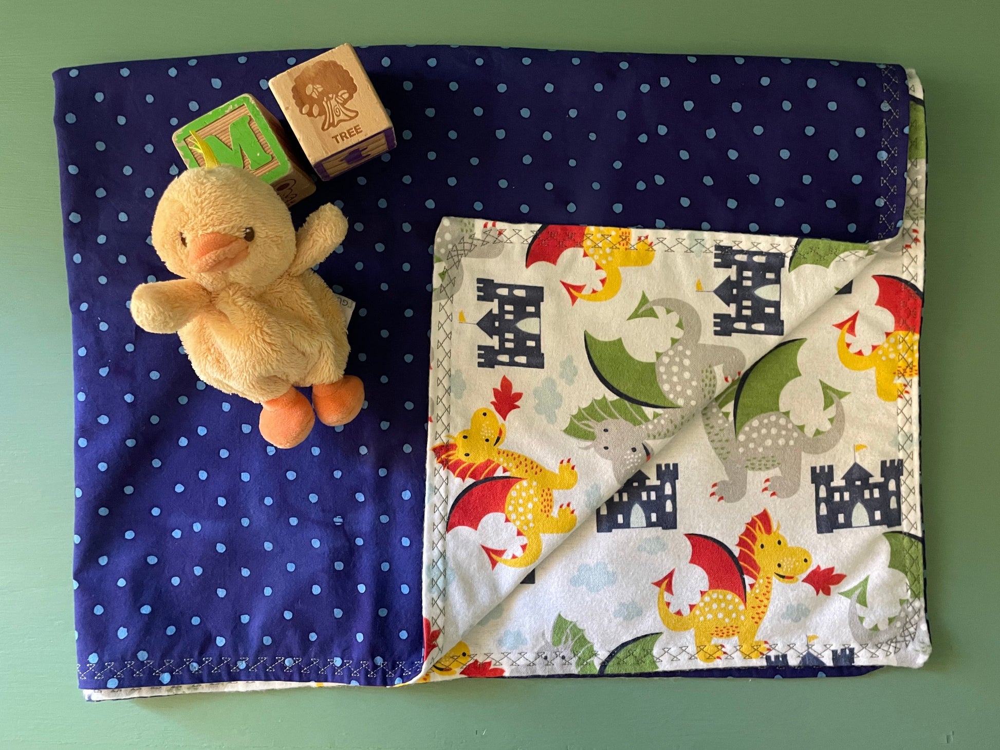 Children's reversible blanket with dragon design on one side and blue polka dot fabric on the reverse