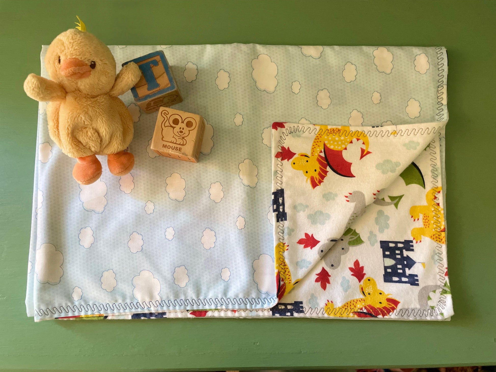 Baby blanket with cloud pattern and toy on a green surface