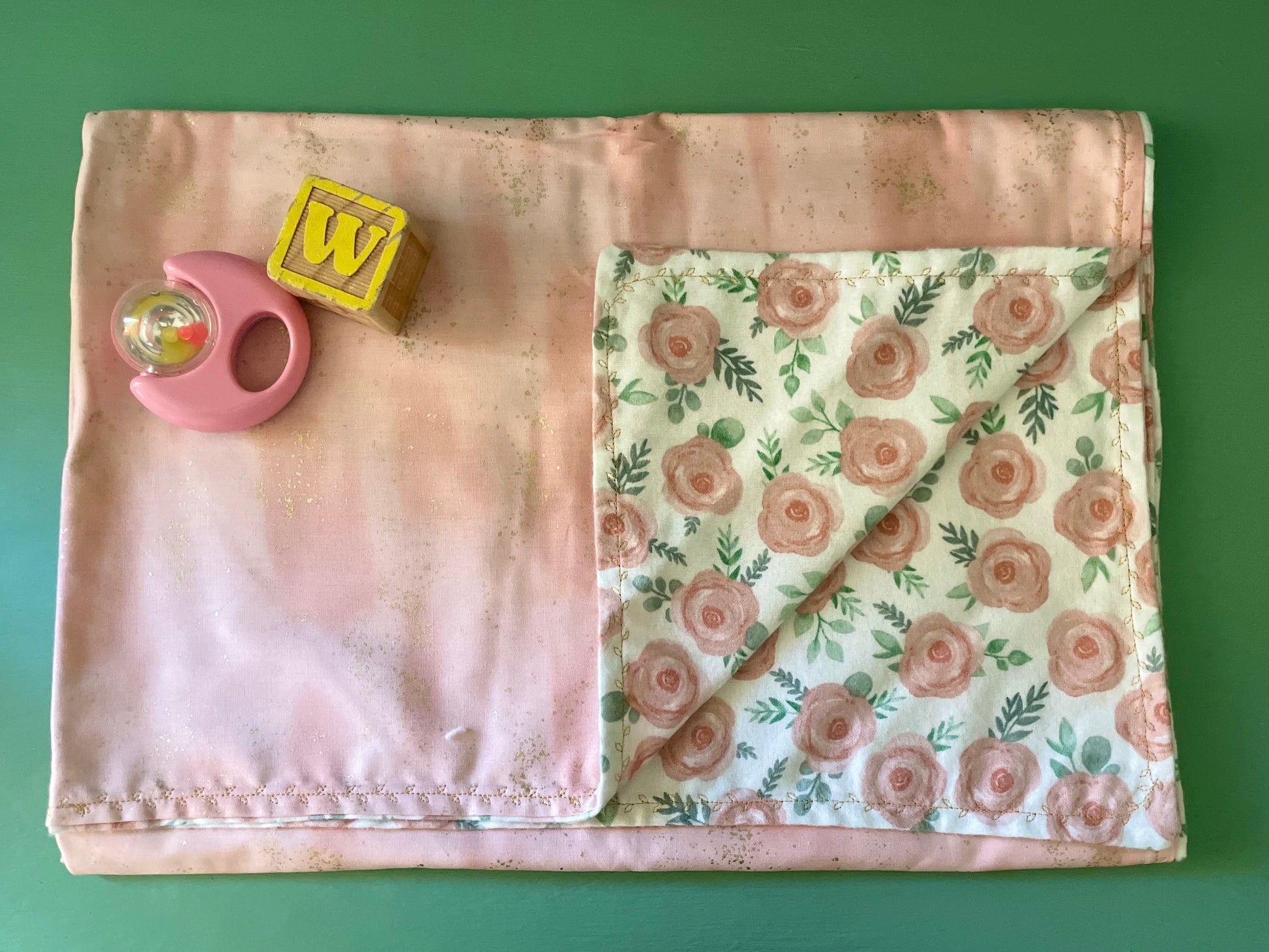 Reversible baby blanket with floral pattern on one side and pink fabric on the reverse