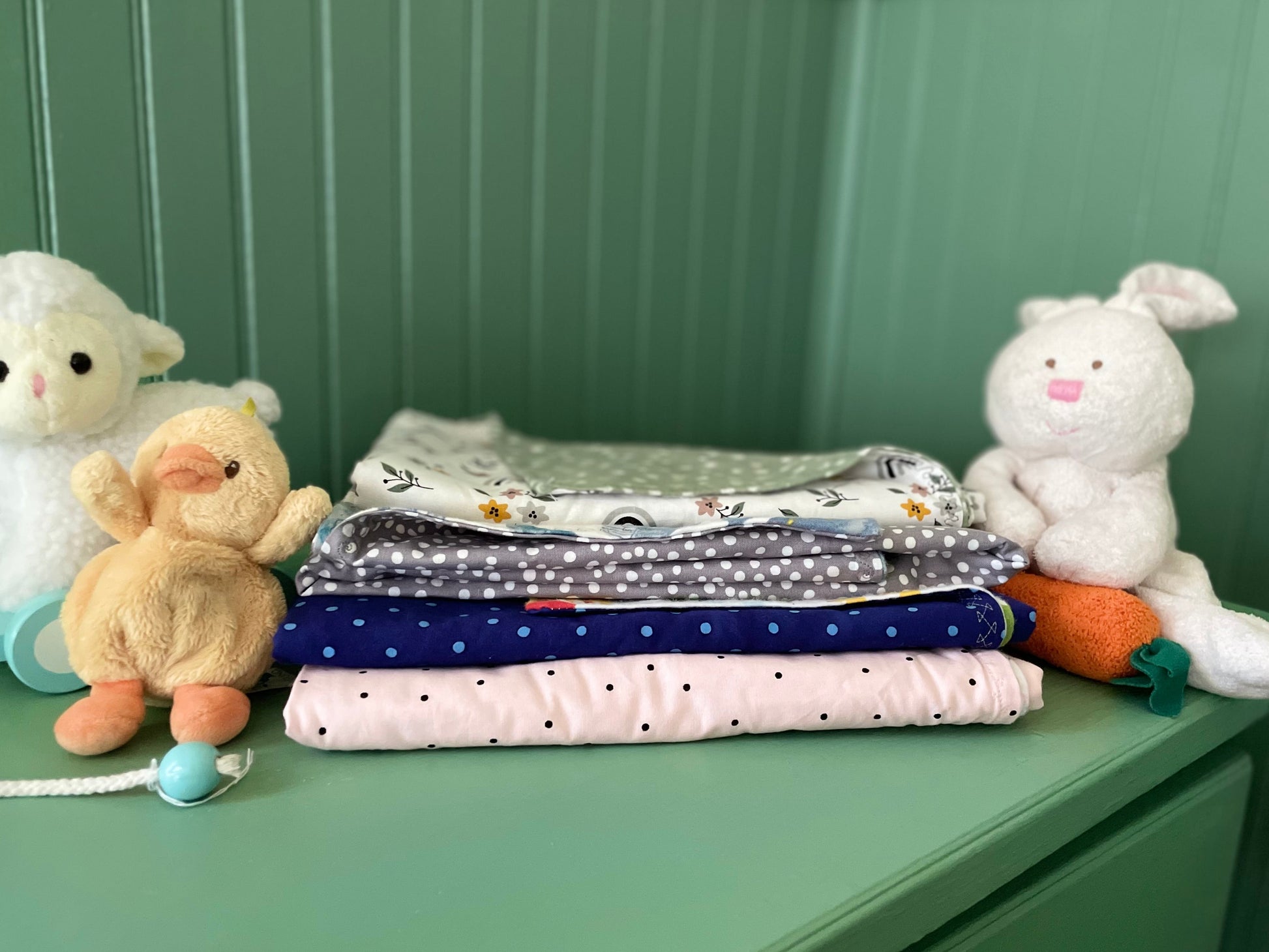 Stack of baby blankets with stuffed animals on a green surface