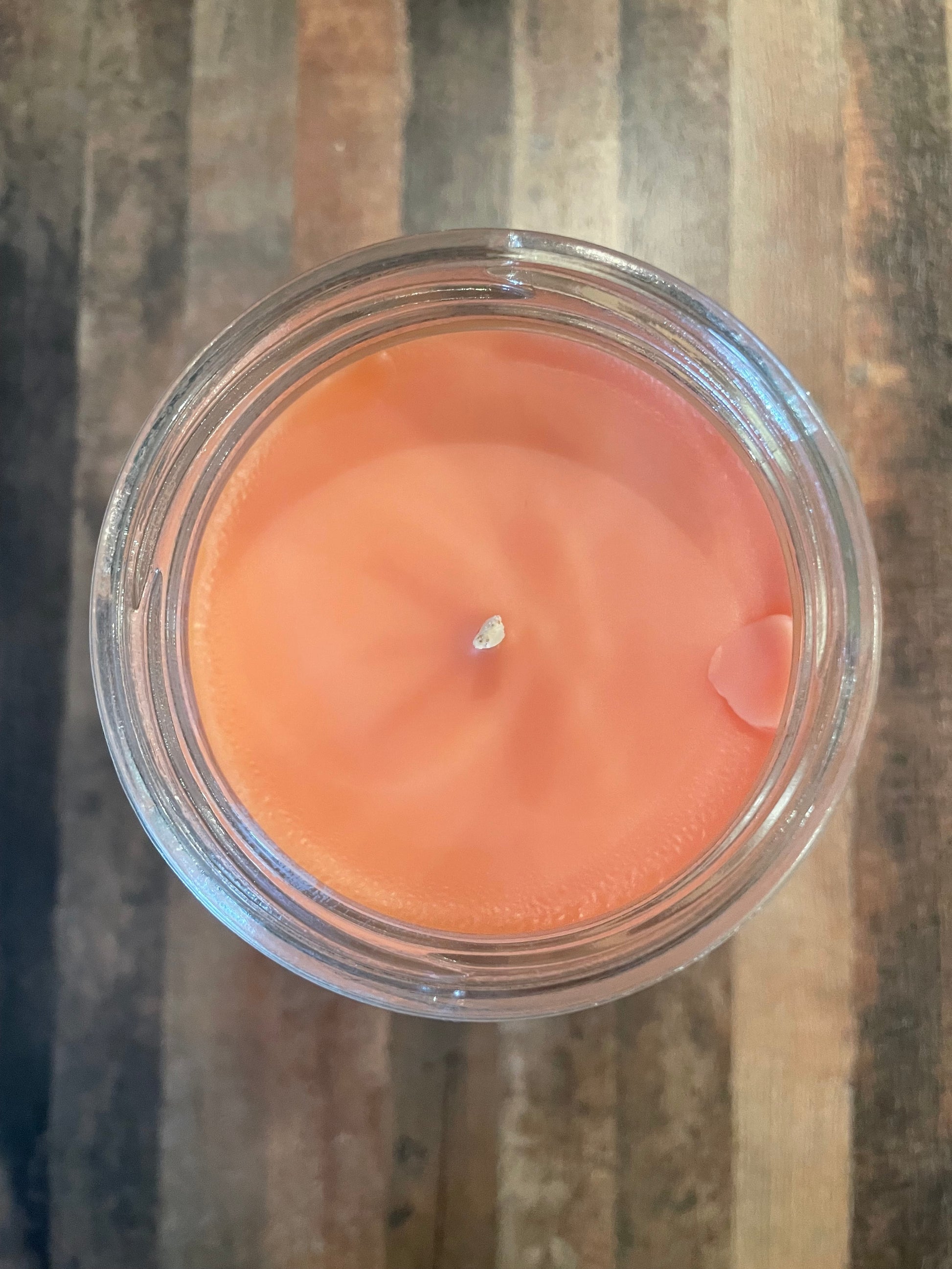 Orange candle in a clear glass jar on a wooden surface