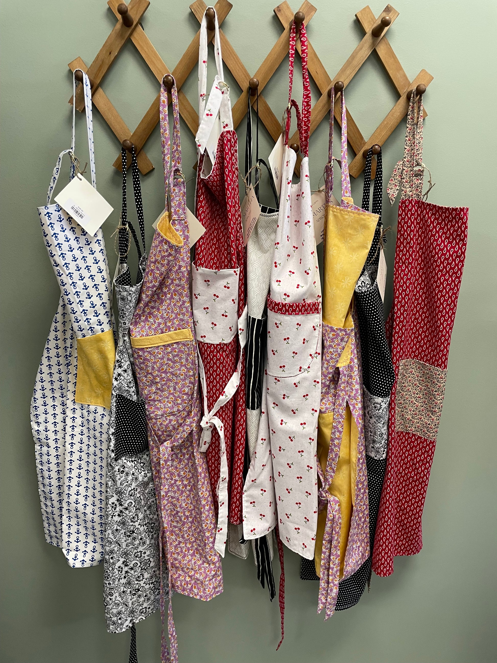 Collection of patterned aprons on a wooden stand against a green background