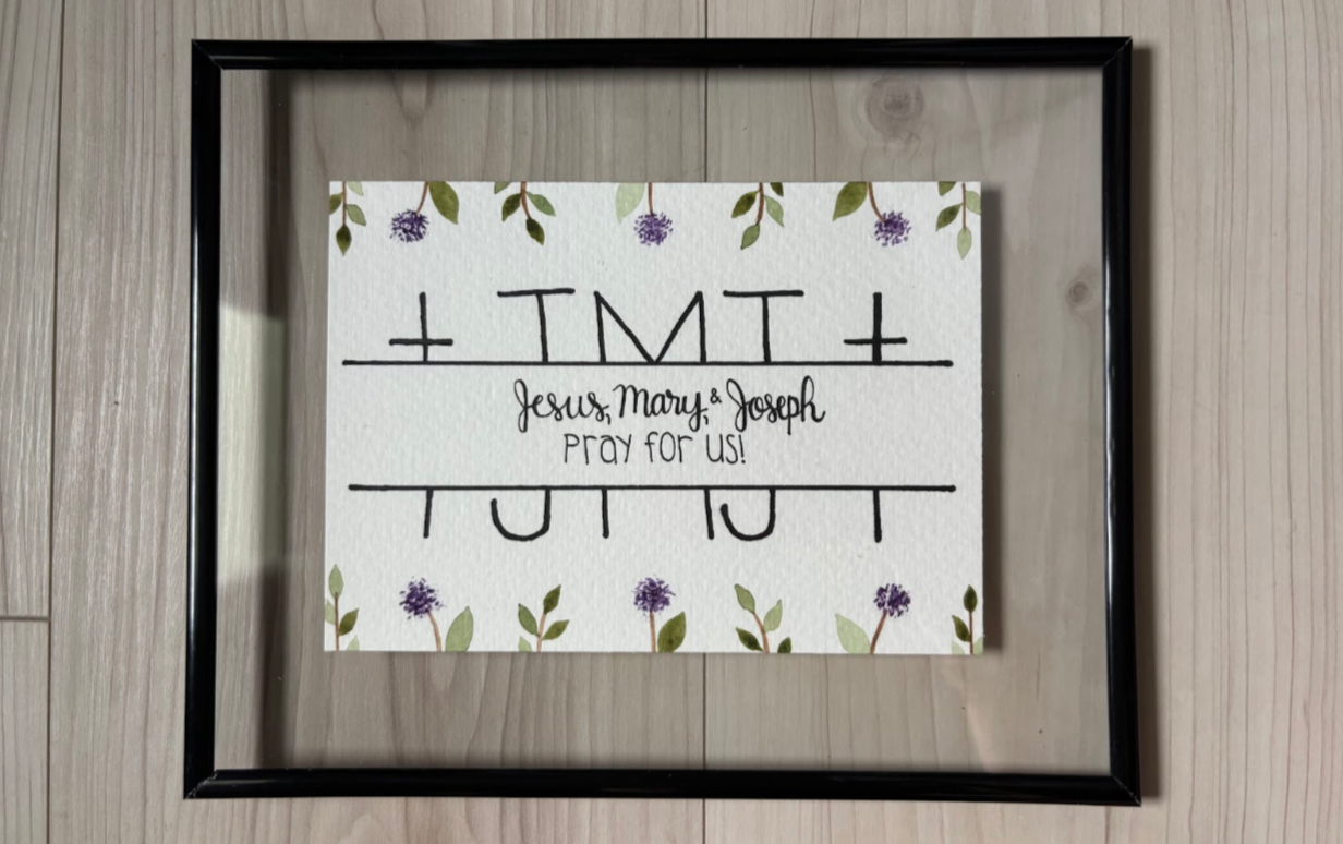 Framed print with religious text and floral design on a wooden surface