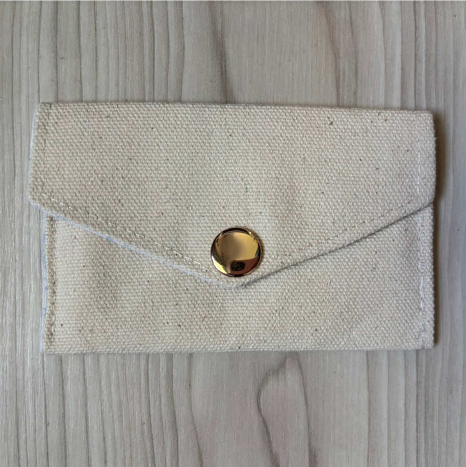 Beige fabric pouch with a gold button on a wooden surface