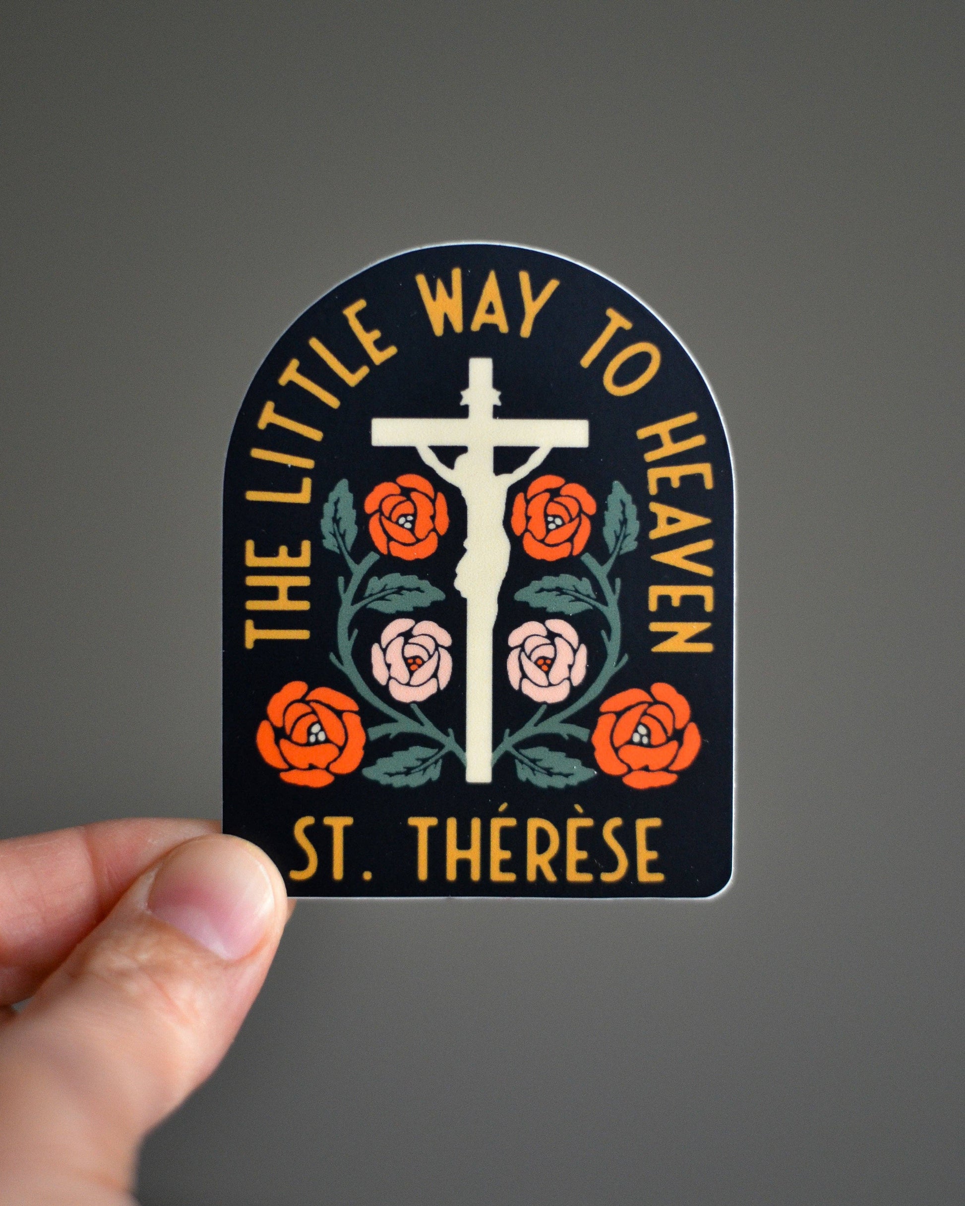 Sticker with cross and flowers held by a hand against a gray background