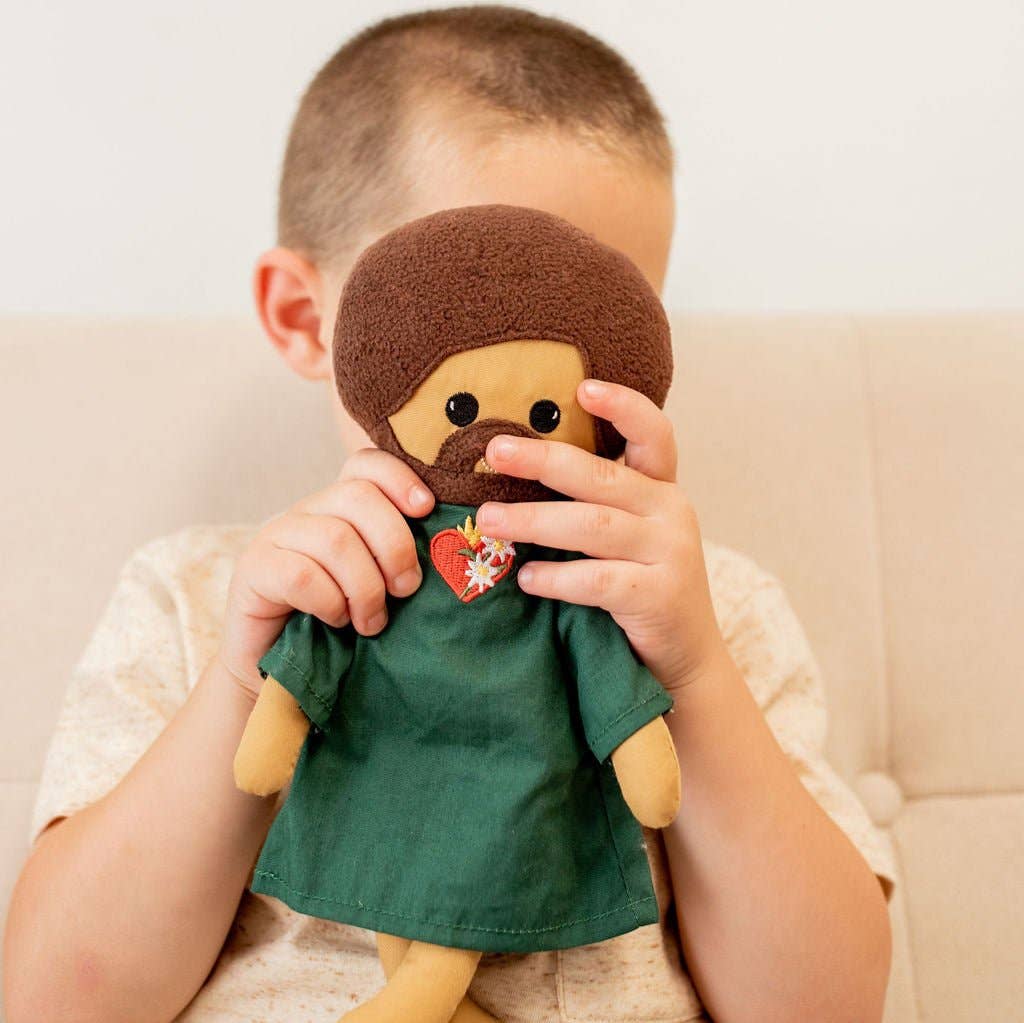 Child holding a plush toy with a beard and green shirt against a neutral background