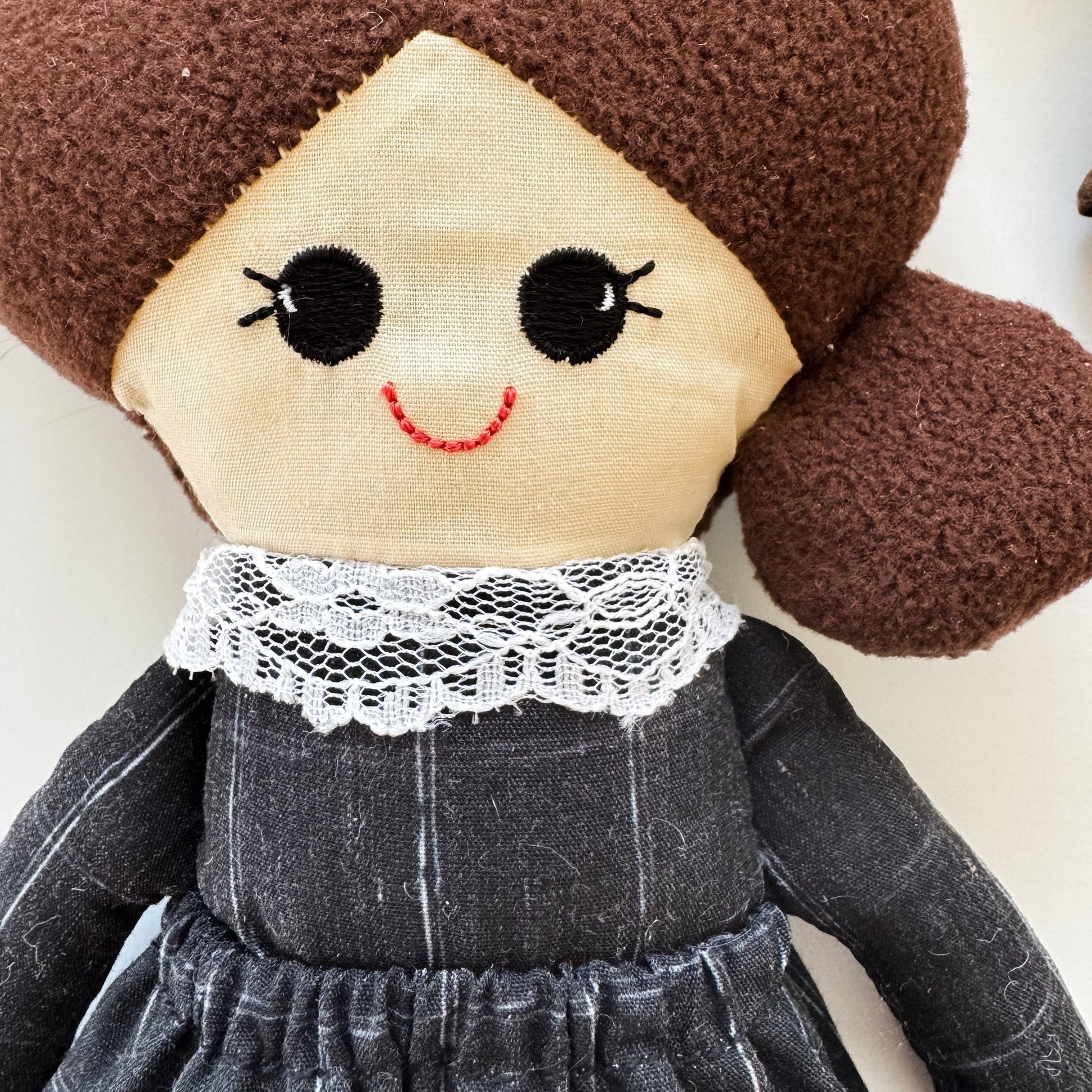 Plush toy with a smiling face, brown hair, and black dress on a white background