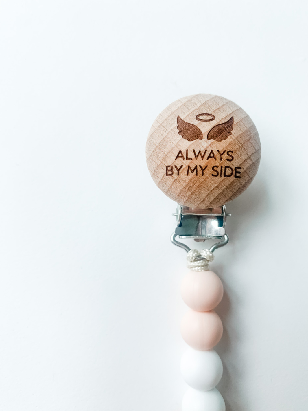 Wooden pacifier clip with 'Always by my side' text on a white background