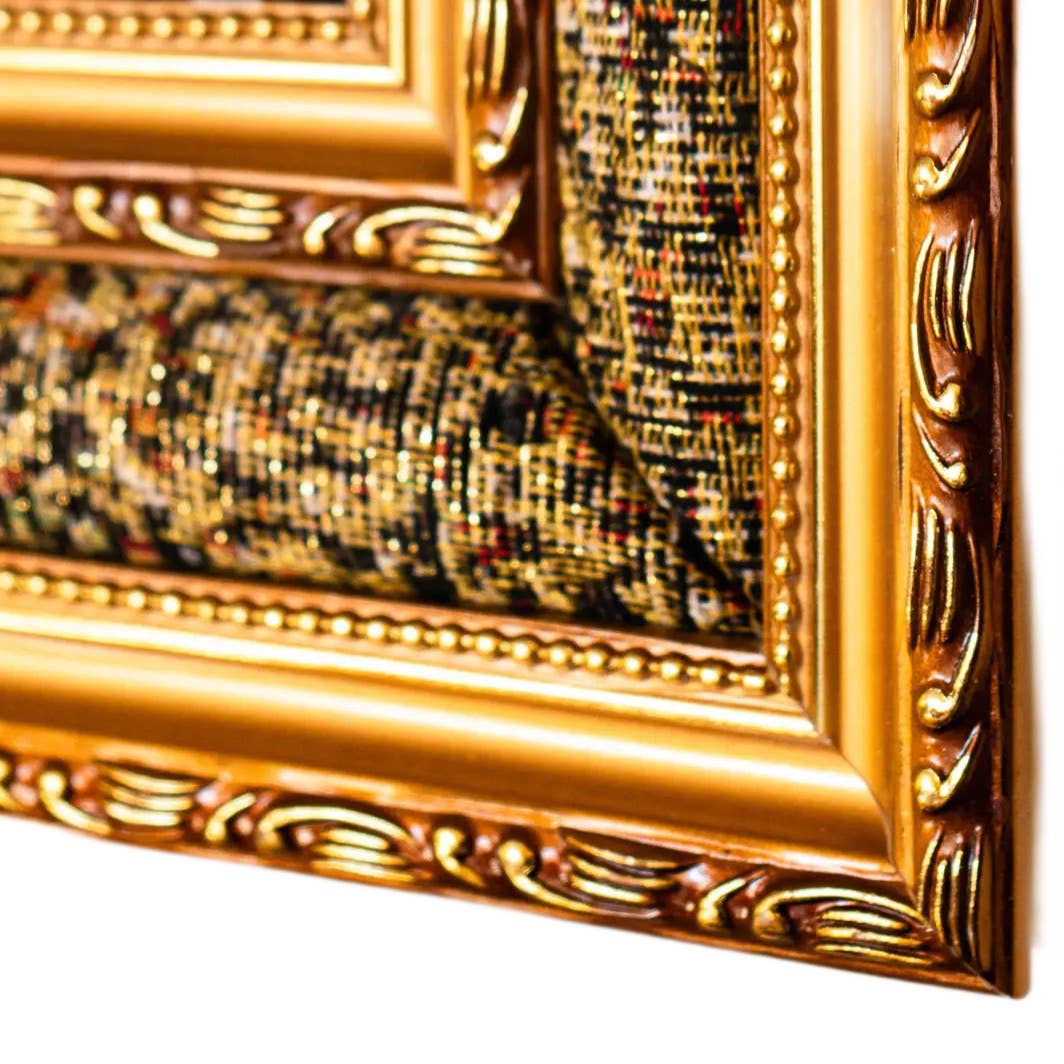 Close-up of a gold ornate picture frame with a textured fabric background.