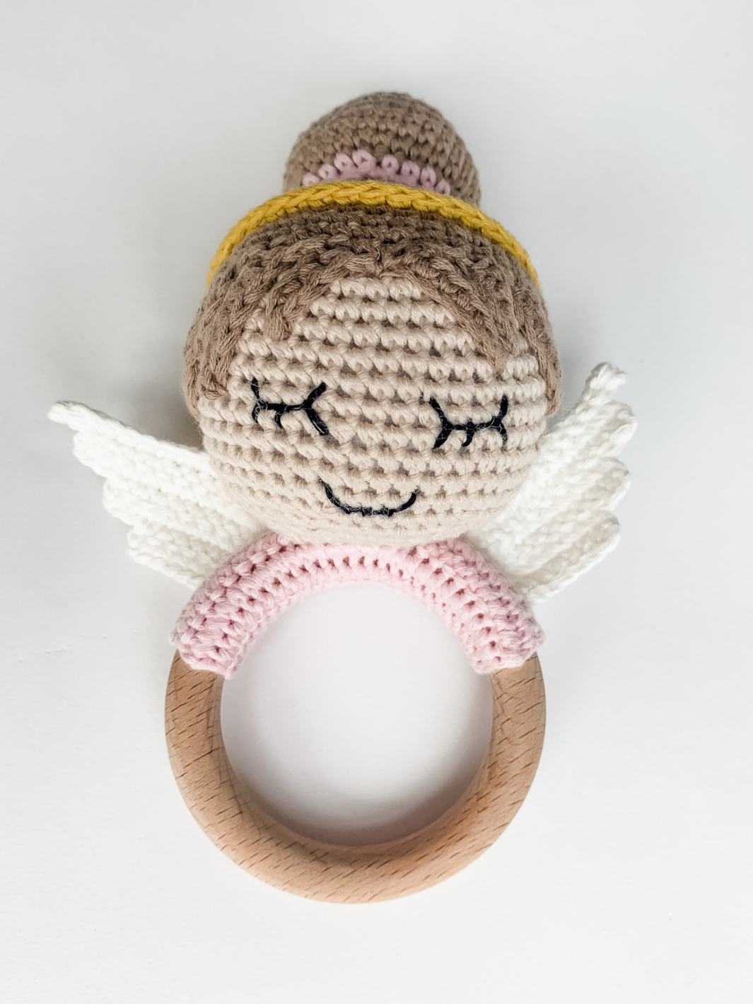Crocheted angel rattle with wooden ring on a white background