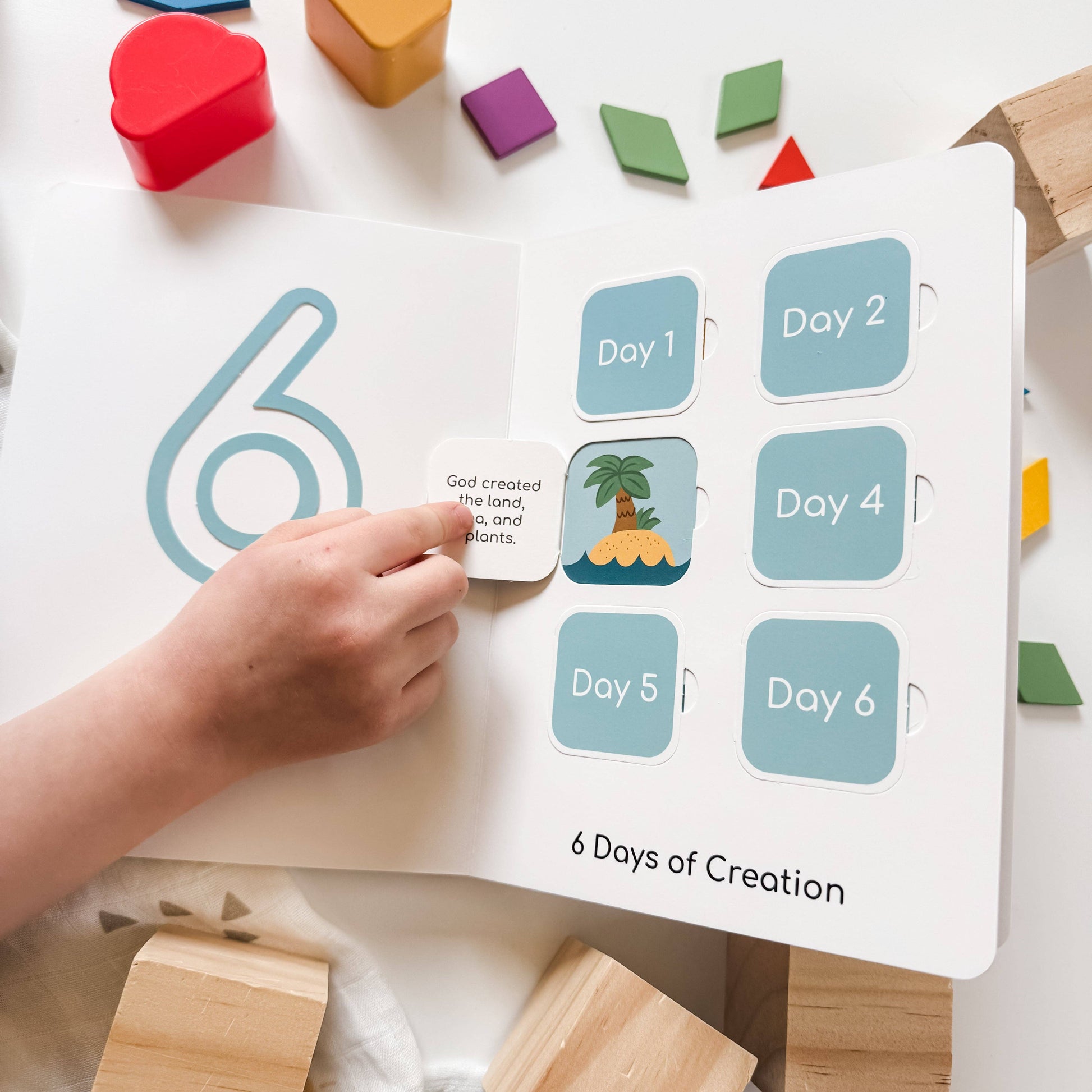 Children's educational book titled '6 Days of Creation' with colorful blocks on a white surface.