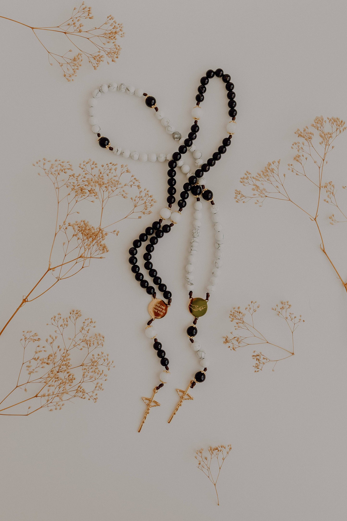Black and white beaded rosary’s on a light background with dried flowers.