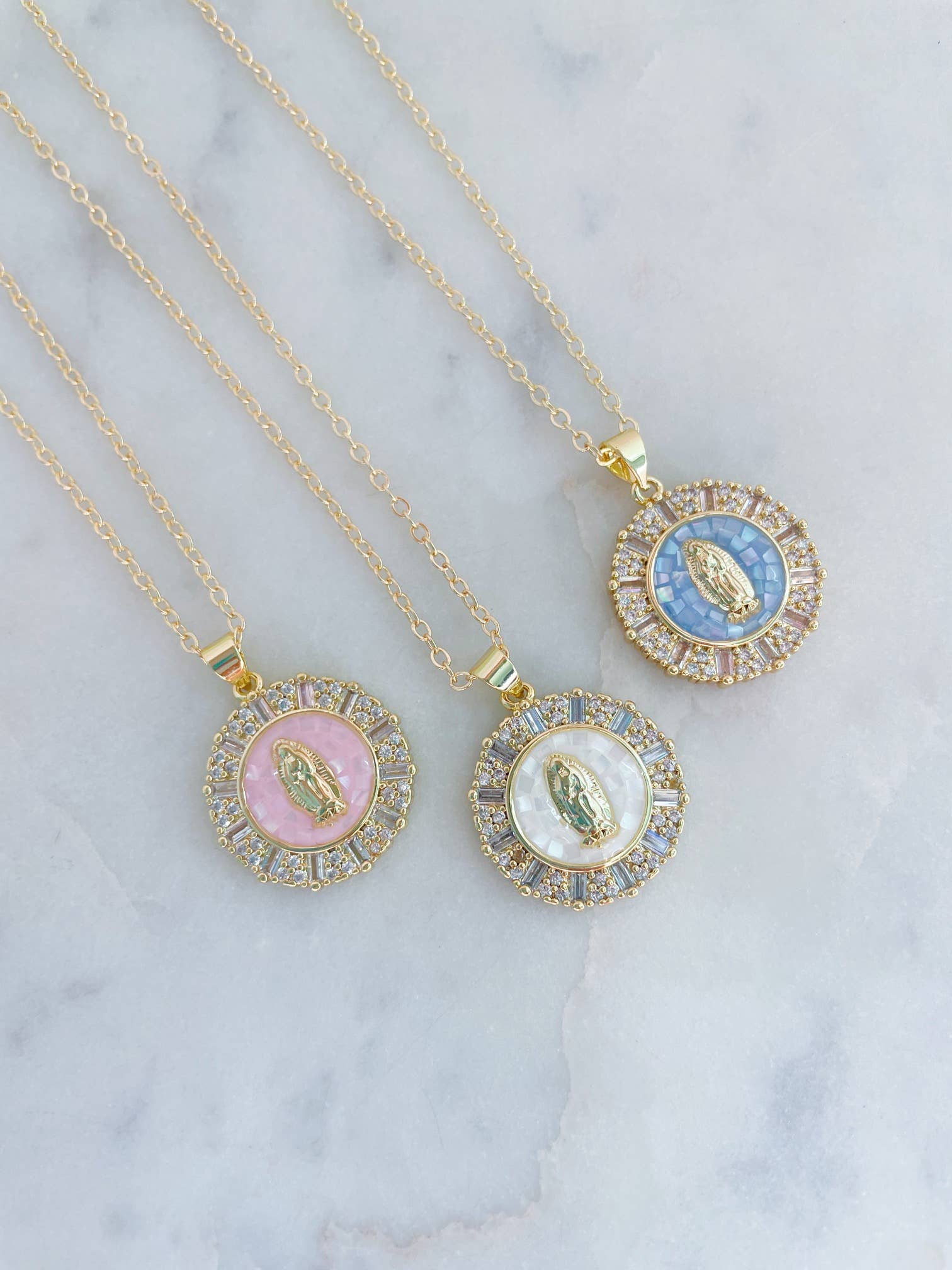 Three gold necklaces with circular pendants on a marble surface