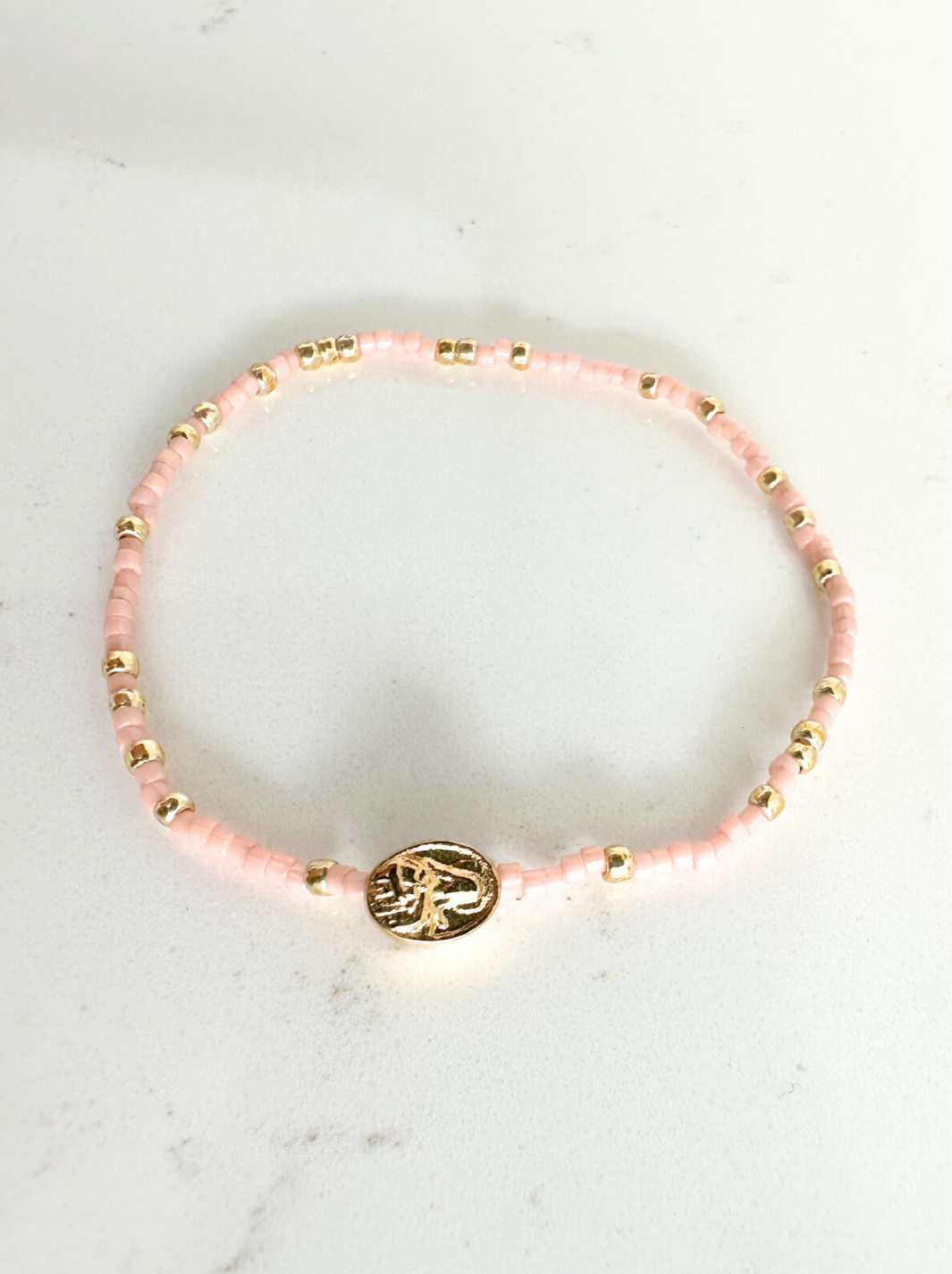Pink beaded bracelet with a gold charm on a white marble surface