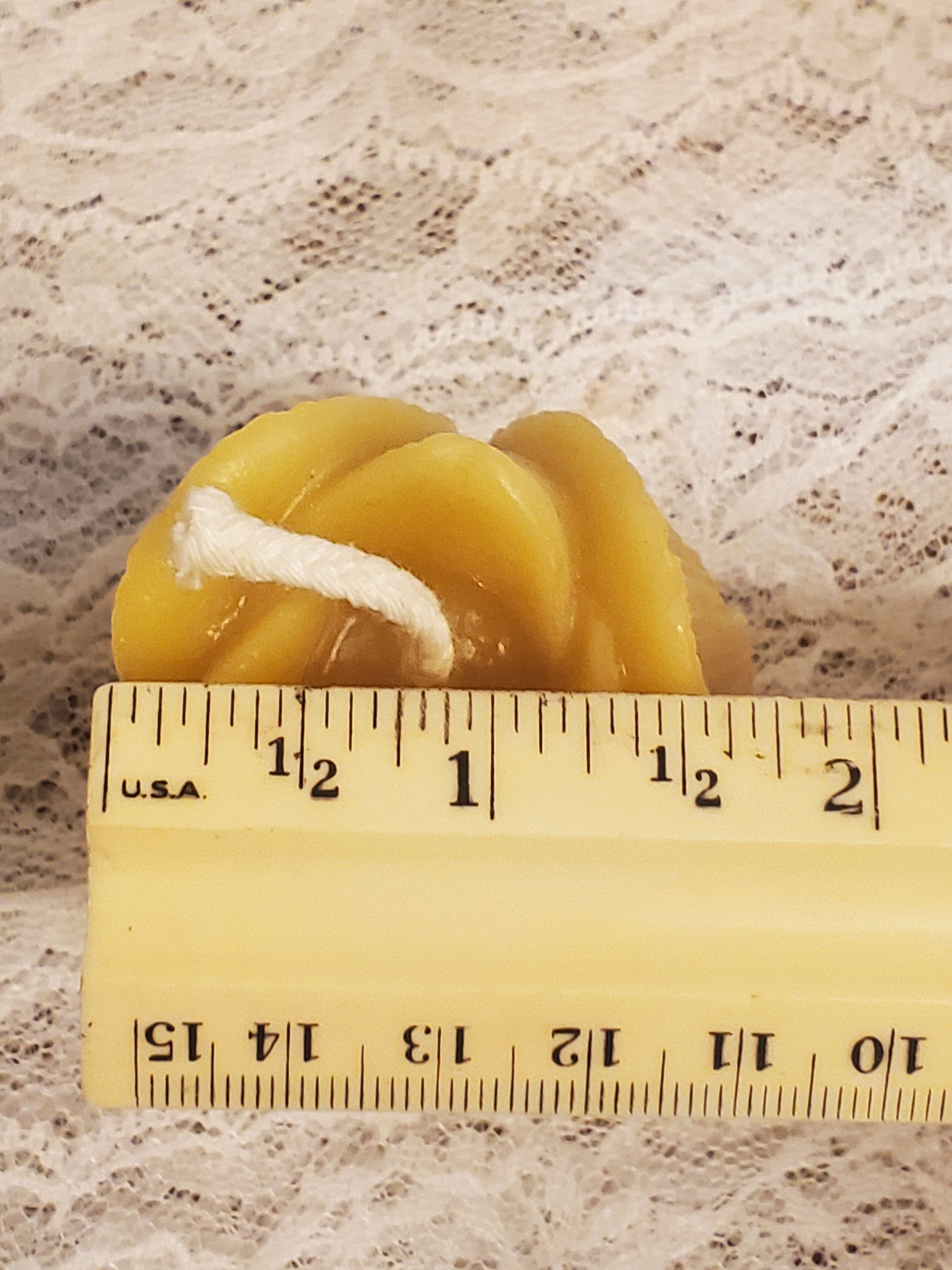 Yellow candle with a wick next to a ruler on a textured surface