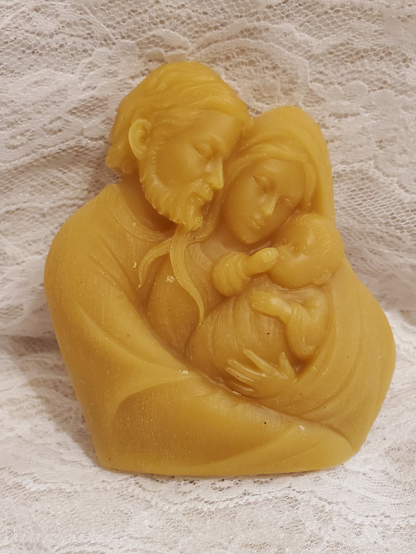 Yellow wax mold with intricate design  of the Holy Family on a textured beige surface
