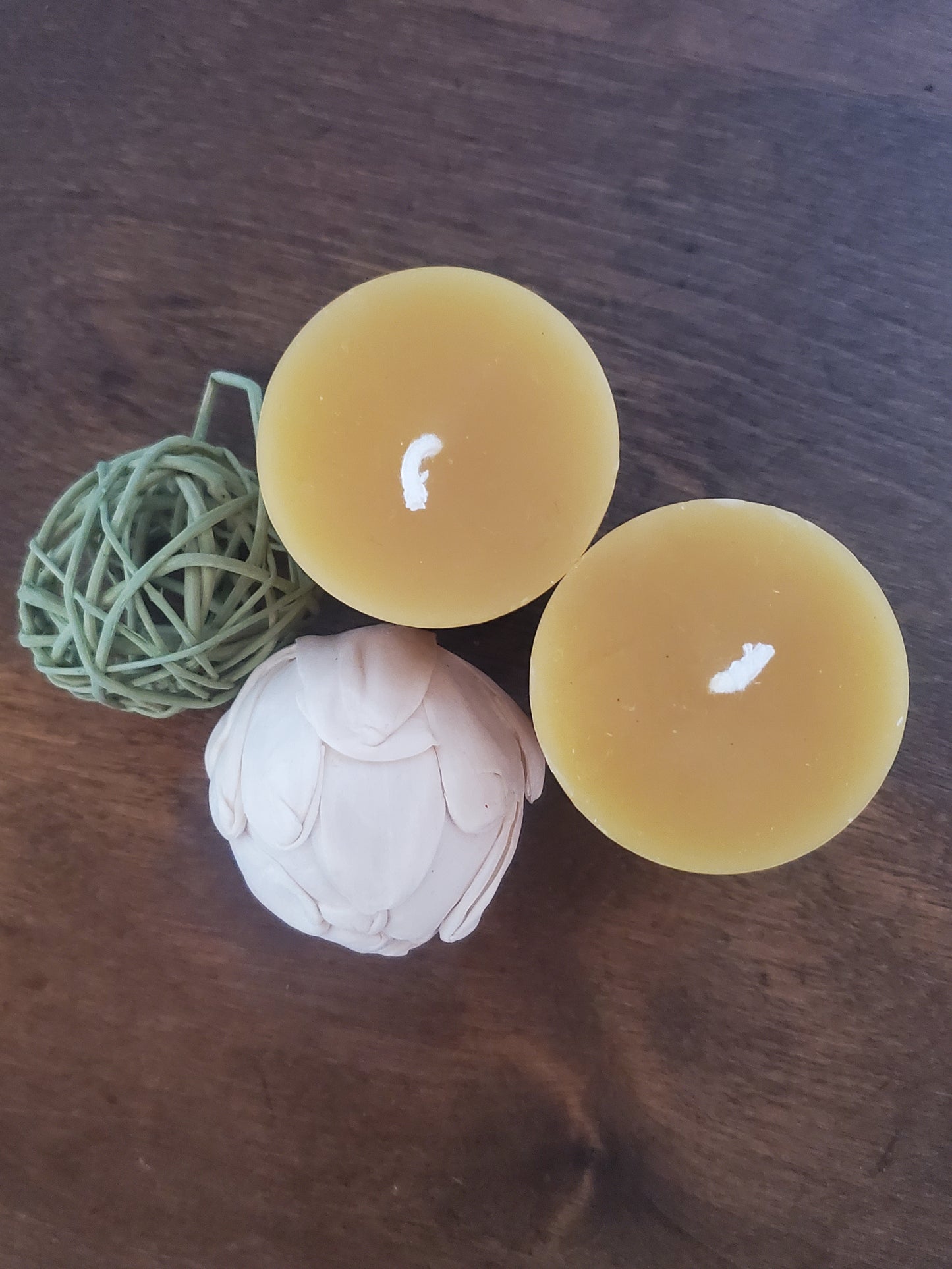 Two round beeswax candles on a wooden surface.