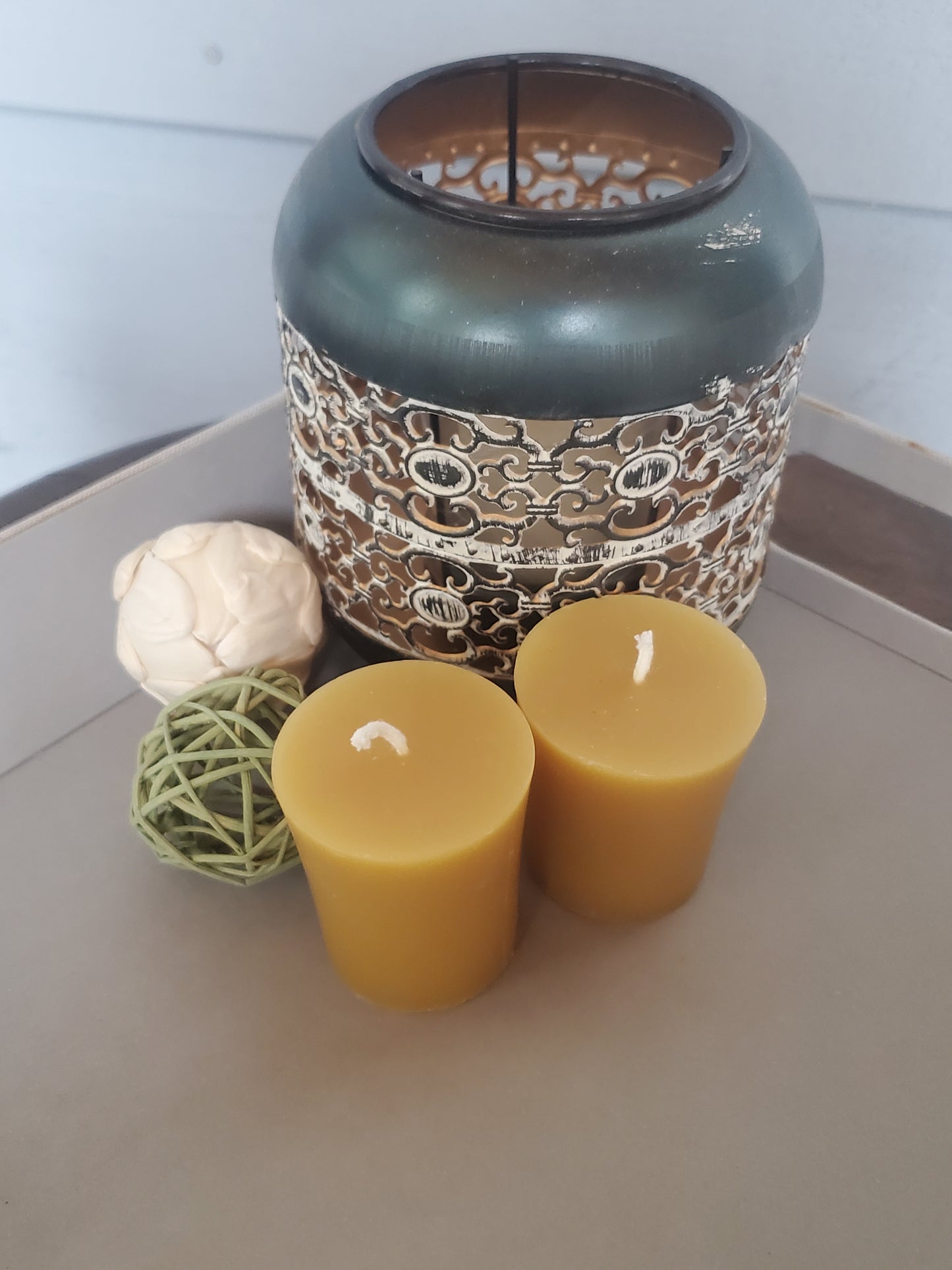 Decorative items including a textured vase, beeswax candles, and spherical objects on a light surface.
