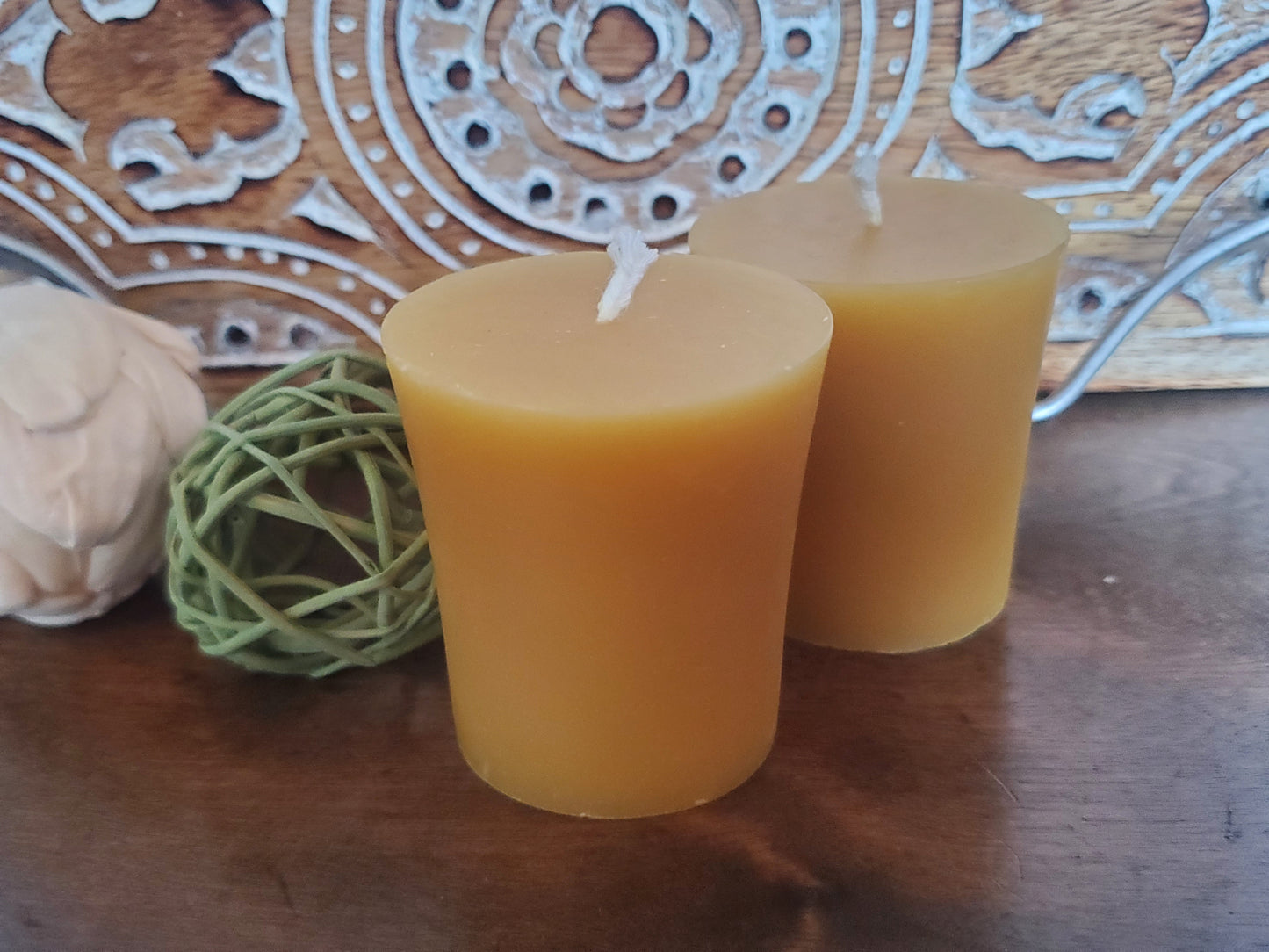 Two beeswax candles on a wooden surface with decorative elements in the background.