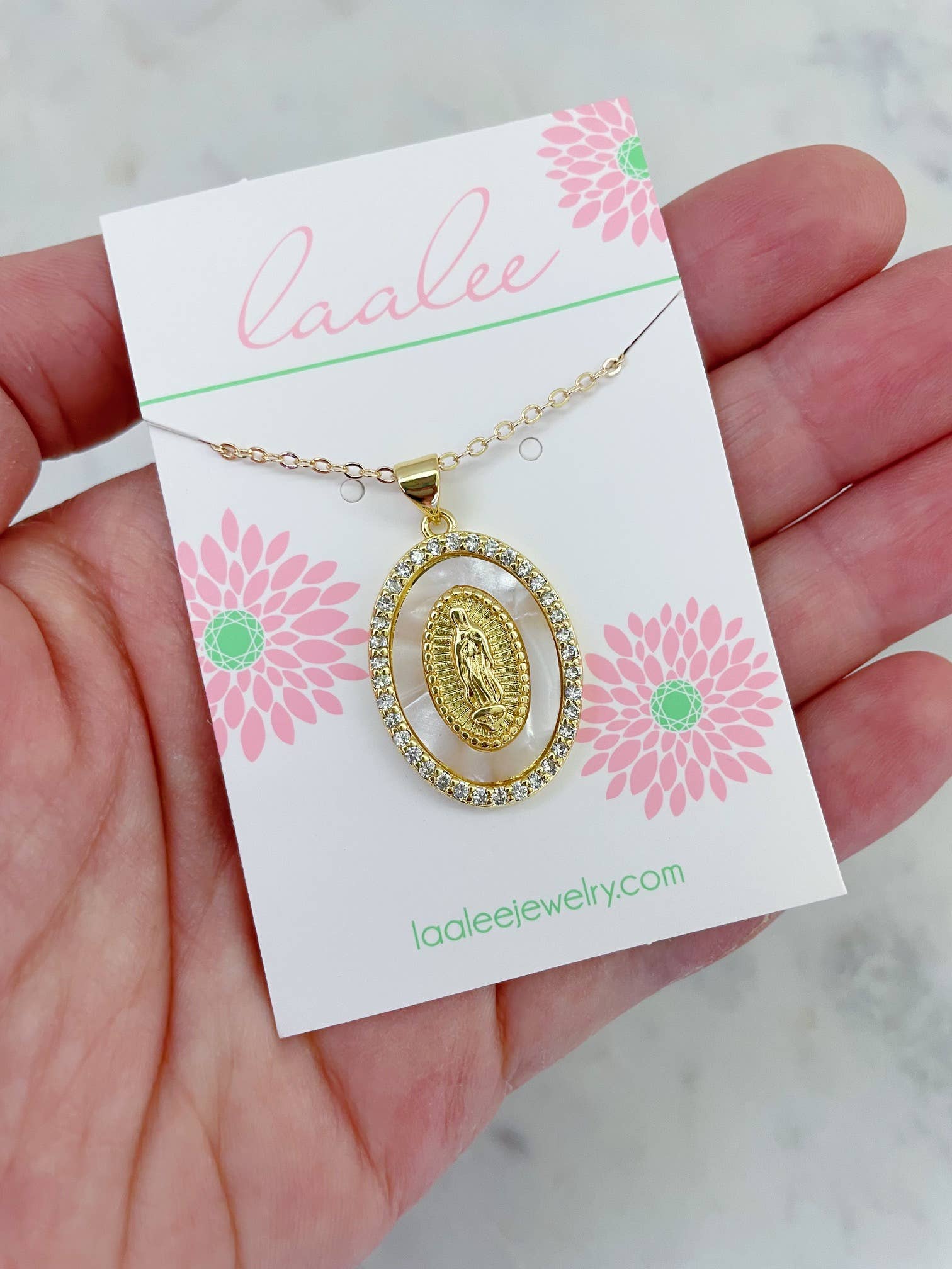 Gold necklace with a pendant on a 'Laalee' branded card held by a hand.
