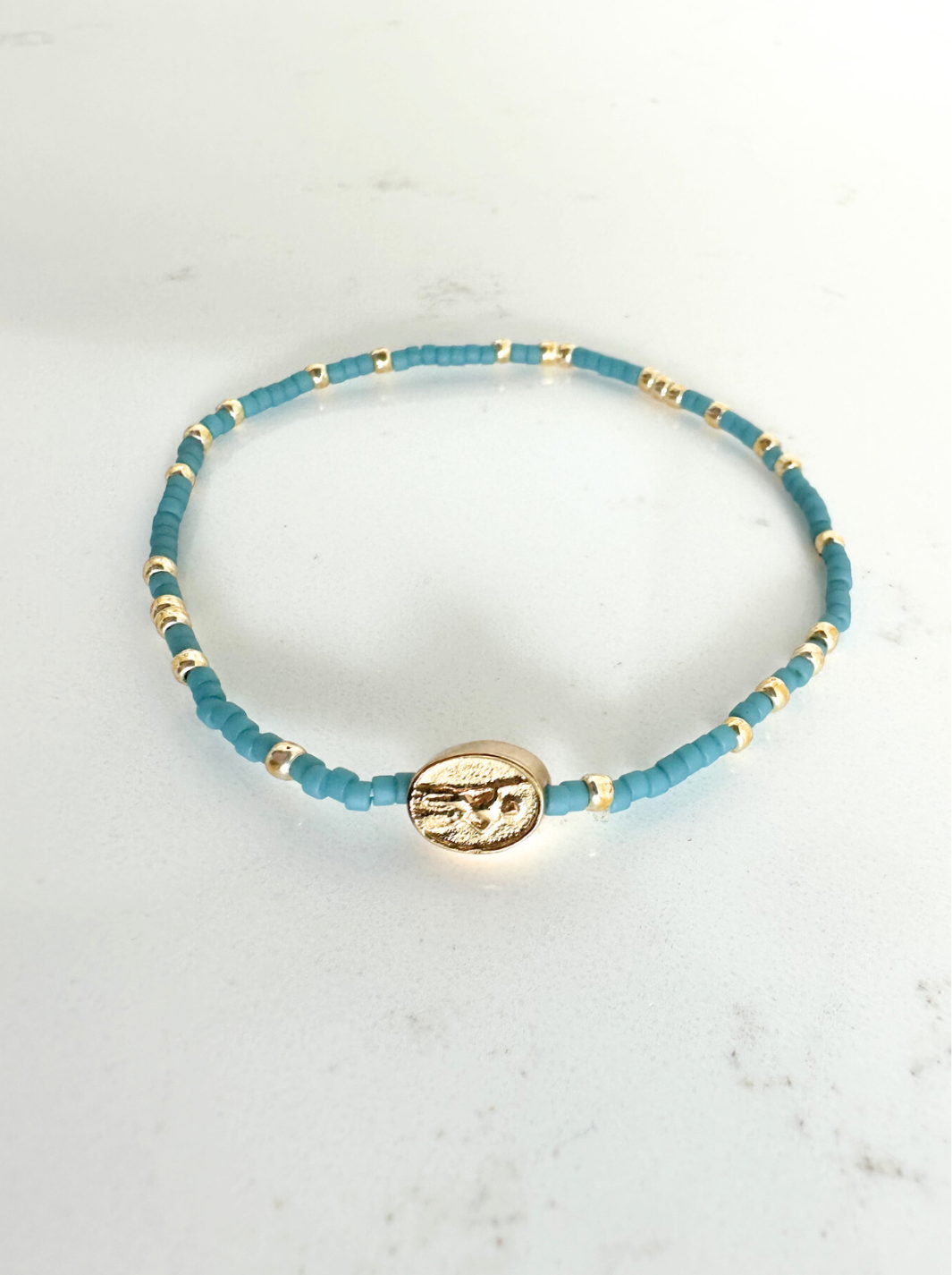 Blue beaded bracelet with a gold charm on a white marble surface
