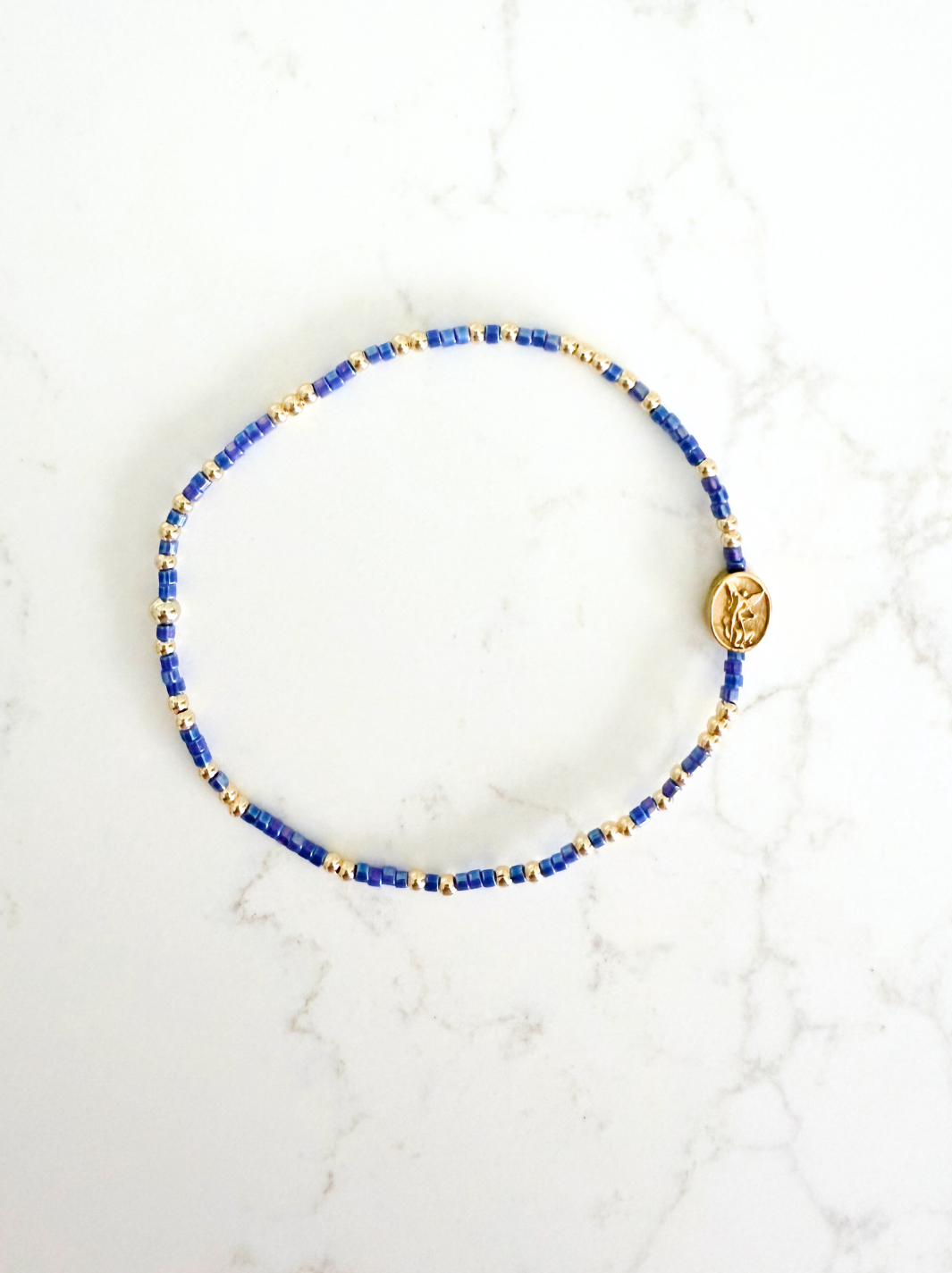 Bracelet with blue and gold beads on a white marble surface