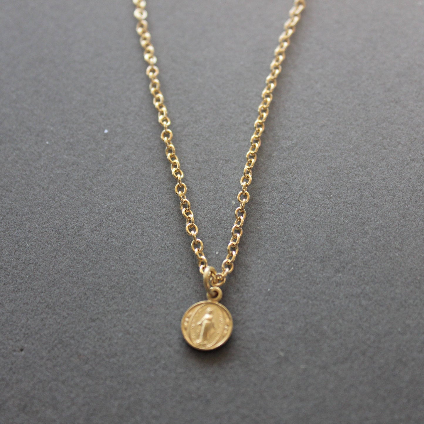 Gold necklace with a round pendant on a gray background
