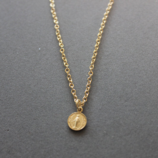 Gold necklace with a round pendant on a gray background